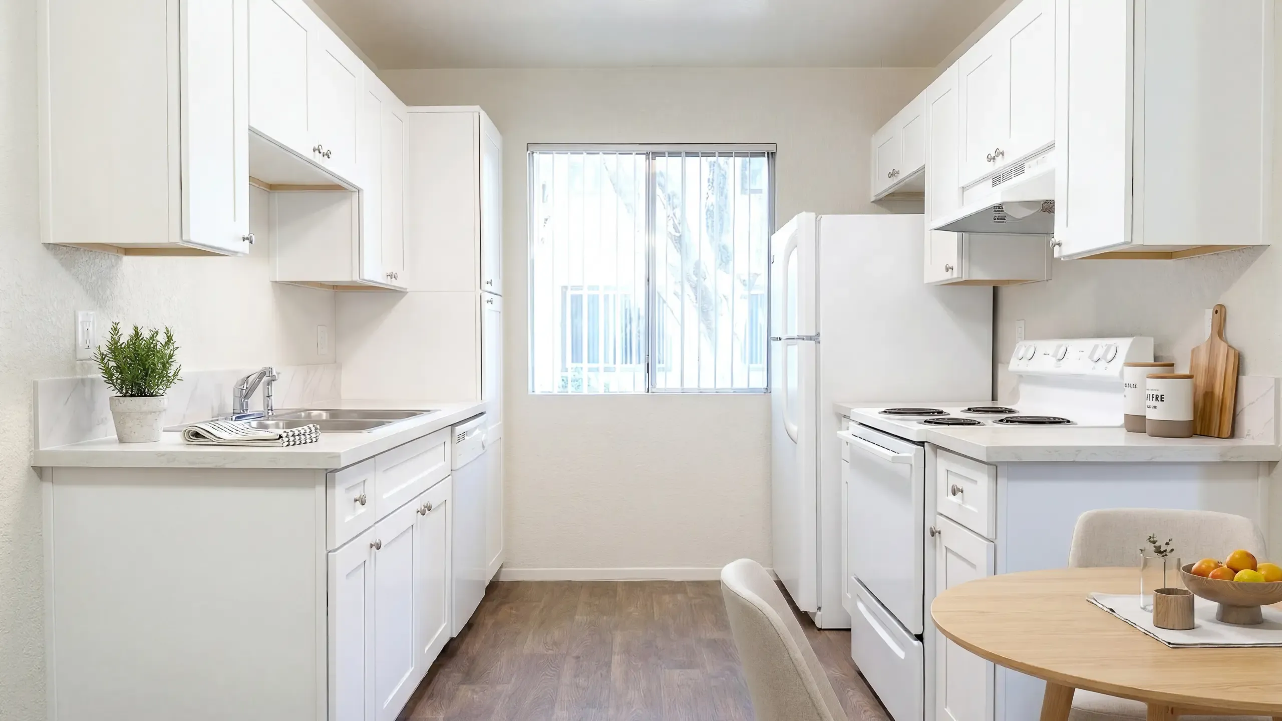 Bright and inviting kitchen at Camelot Apartments with modern white cabinets, sleek countertops, and warm wood flooring, perfect for culinary adventures.