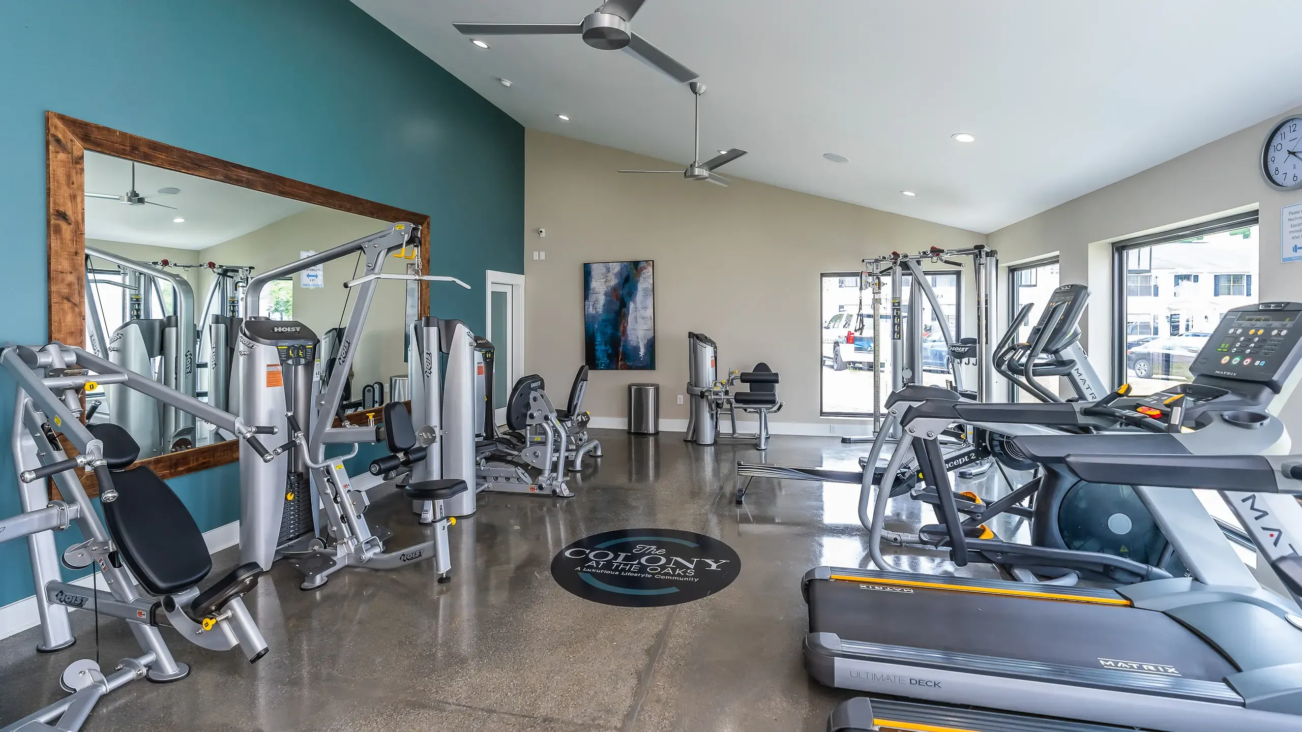 Bright and modern fitness center at The Colony at the Oaks Apartments featuring state-of-the-art equipment and large mirrors, perfect for an energizing workout experience.