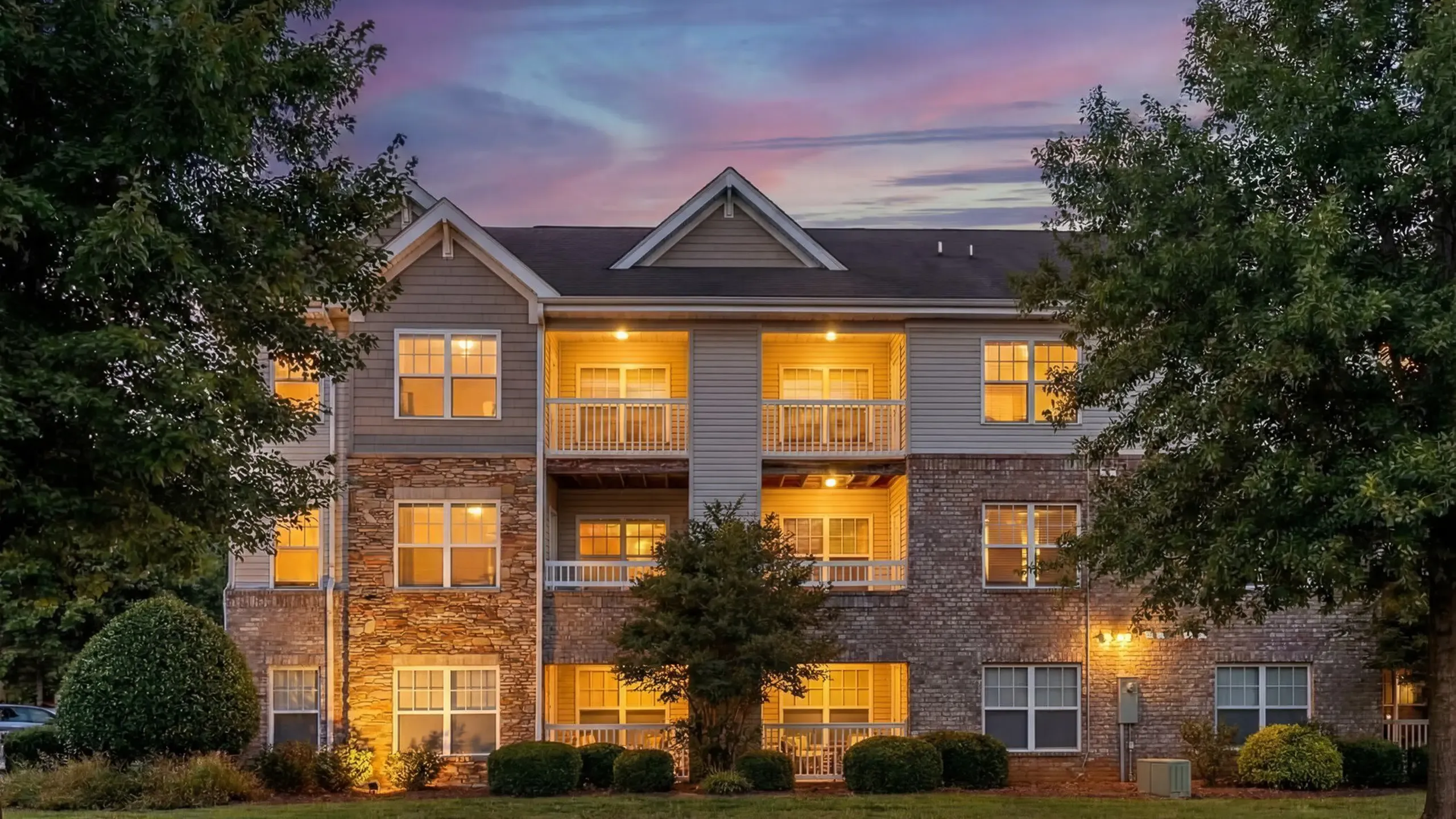Charming apartment building with stone and brick facade, surrounded by lush greenery and vibrant trees at Stratford at Hillcrest Apartments in Winston-Salem.