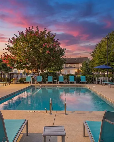 Inviting pool area with luxurious loungers, surrounded by lush greenery and vibrant sunset skies, perfect for outdoor relaxation.