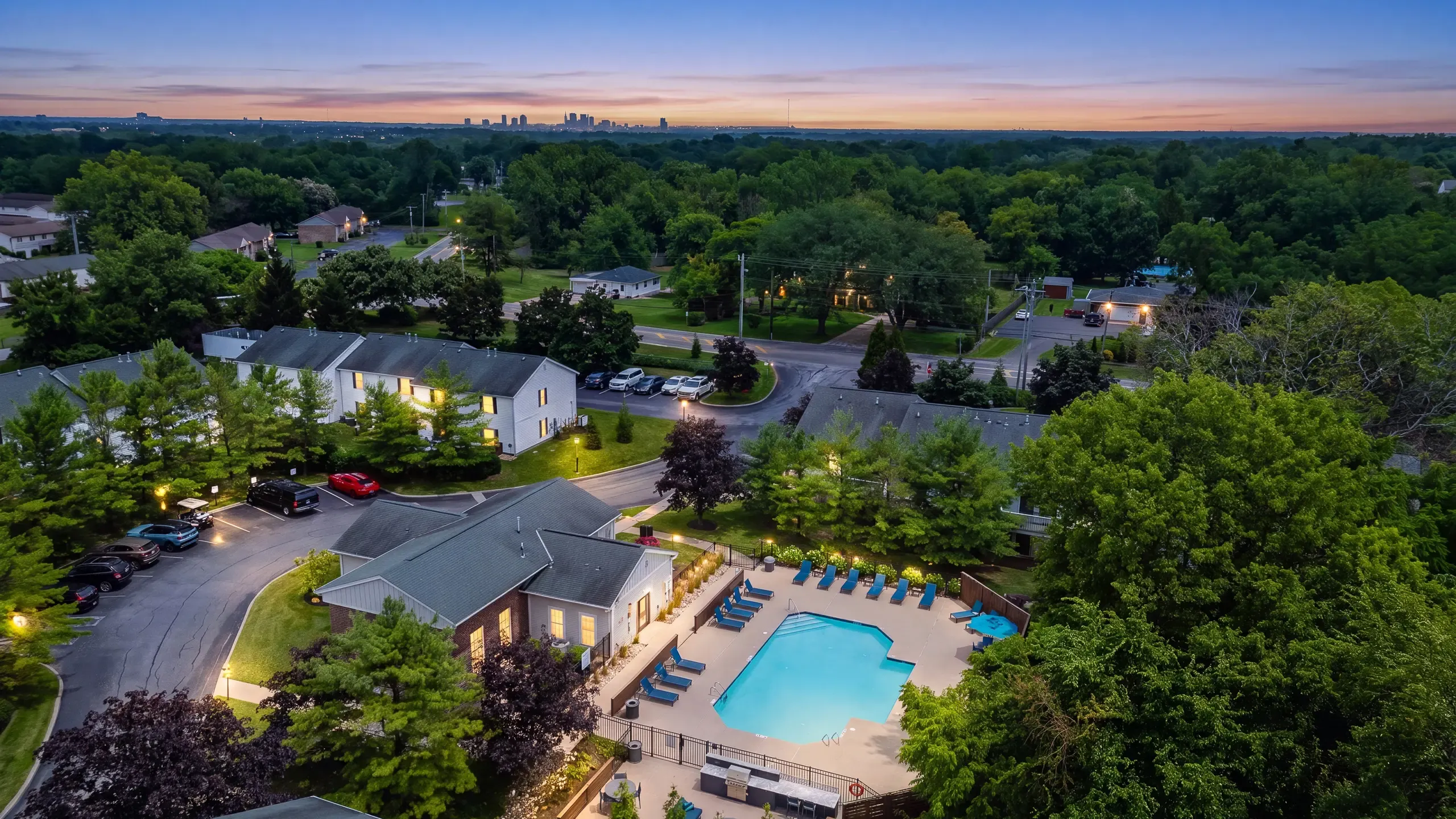 Charming apartment community at sunset with a refreshing pool, surrounded by lush greenery and a serene neighborhood view.