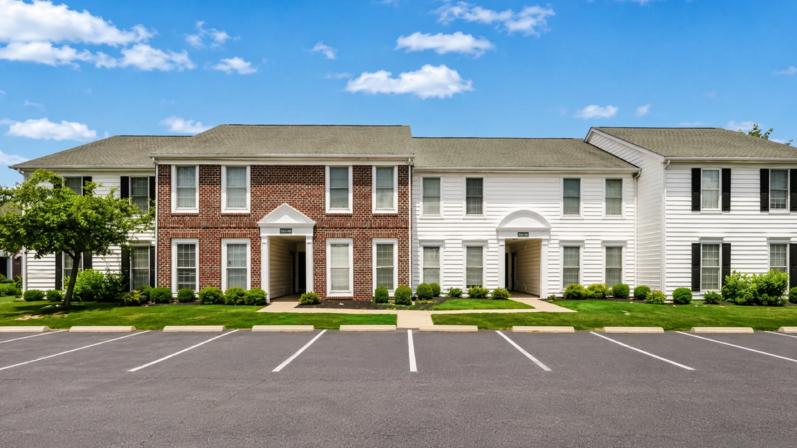 Elegant suburban apartment complex with classic brick and siding fa&ccedil;ade, surrounded by well-maintained greenery and ample parking at Alkire Glen Apartments in Columbus, OH.