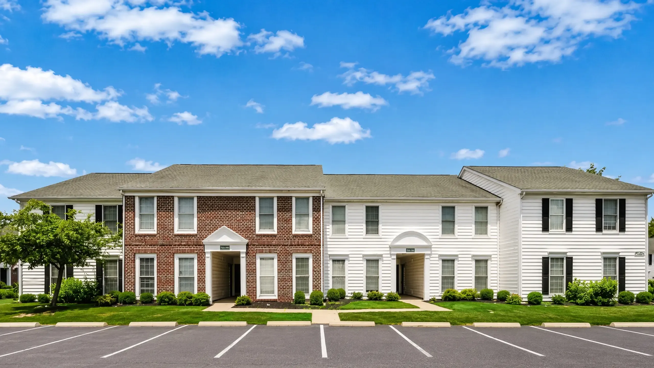 Elegant suburban apartment complex with classic brick and siding fa&ccedil;ade, surrounded by well-maintained greenery and ample parking at Alkire Glen Apartments in Columbus, OH.