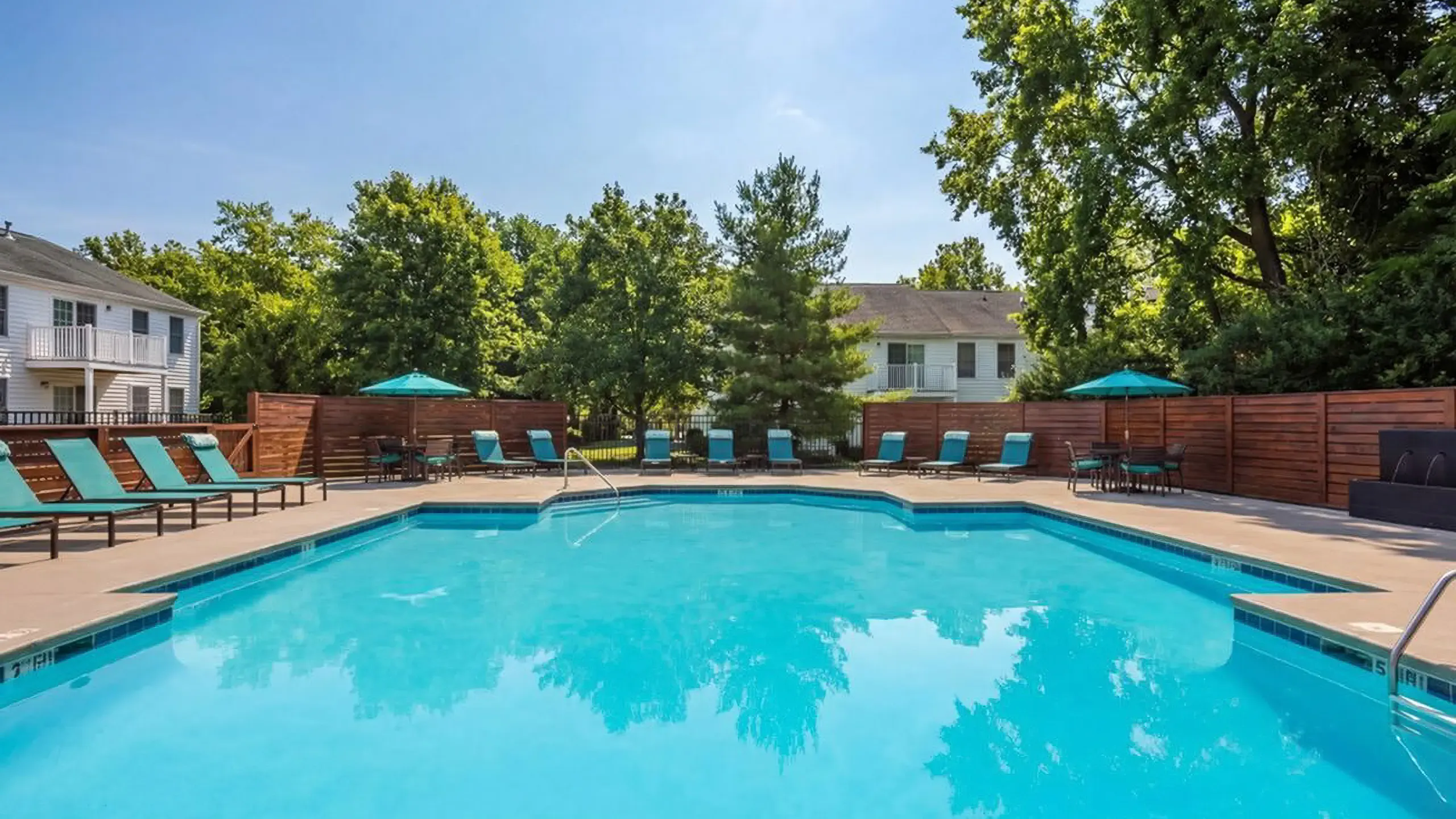 Inviting outdoor pool area with sun loungers and umbrellas, surrounded by lush greenery, perfect for relaxation and leisure at Alkire Glen Apartments