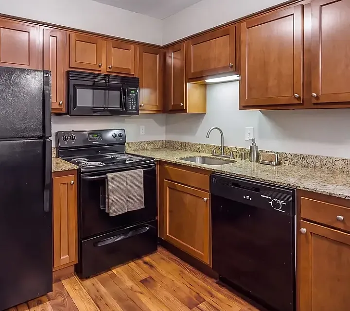 Elegant kitchen at The Creeks on Kirklevington Apartments featuring modern appliances, warm wooden cabinetry, and sleek granite countertops.