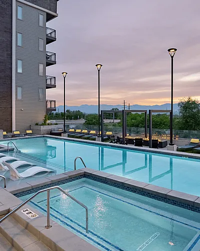 Luxurious apartment complex with a stunning outdoor pool, surrounded by lounge chairs, perfect for relaxation at sunset with scenic mountain views.