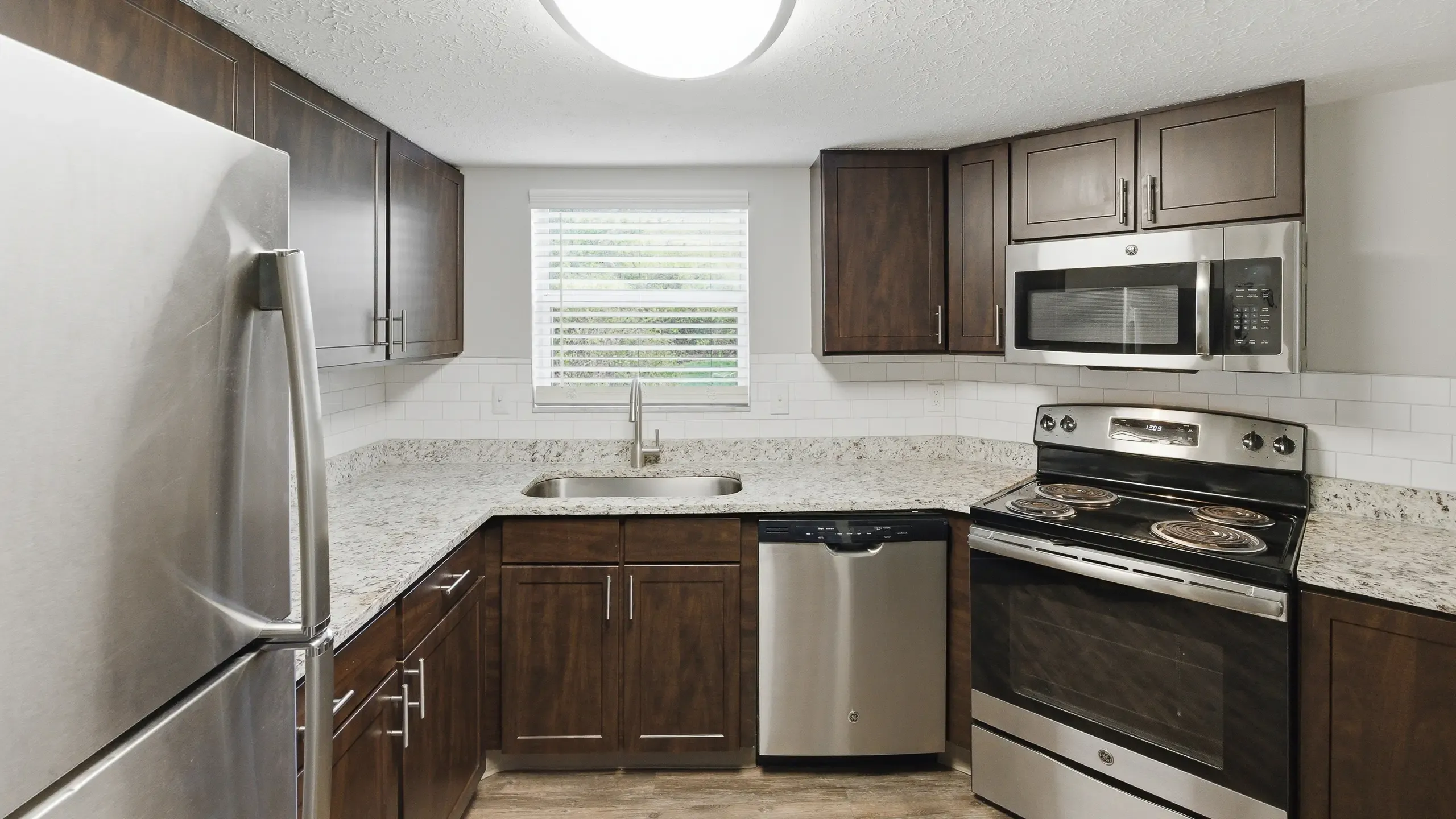 Spacious apartment kitchen featuring dark wood cabinetry, quartz countertops, a white subway tile backsplash, and steel appliances at Retreat at Stillmeadow in Cincinnati, OH.