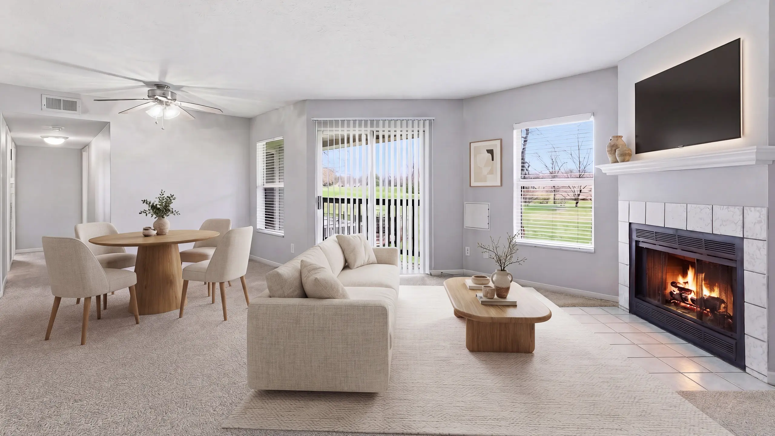 Bright open-concept living room and dining area with large windows, private patio access, and a fireplace at The Retreat at Stillmeadow Apartments in Cincinnati, Ohio.