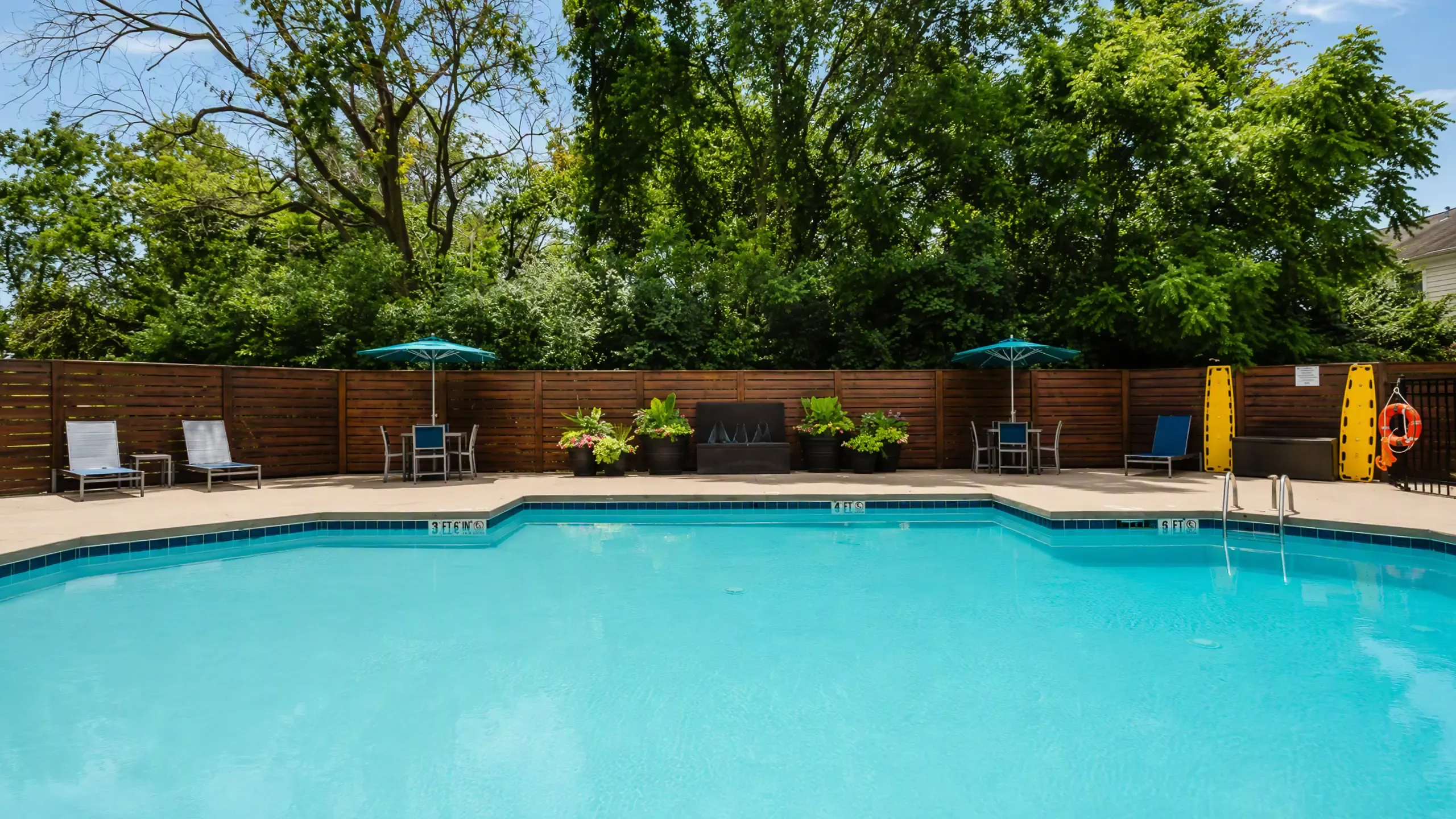 Inviting outdoor pool area with sun loungers and umbrellas, surrounded by lush greenery, perfect for relaxation and leisure at Alkire Glen Apartments