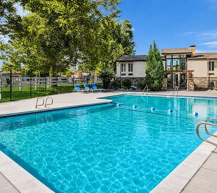 Charming outdoor pool area at Fox Point in Old Farm Apartments with sparkling water, surrounded by lush greenery and a lounge seating.