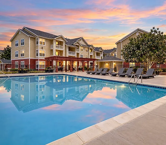 Charming sunset view of a lovely apartment complex, The Orchards at Cherry Creek Park, featuring serene poolside relaxation and elegant lounging chairs.