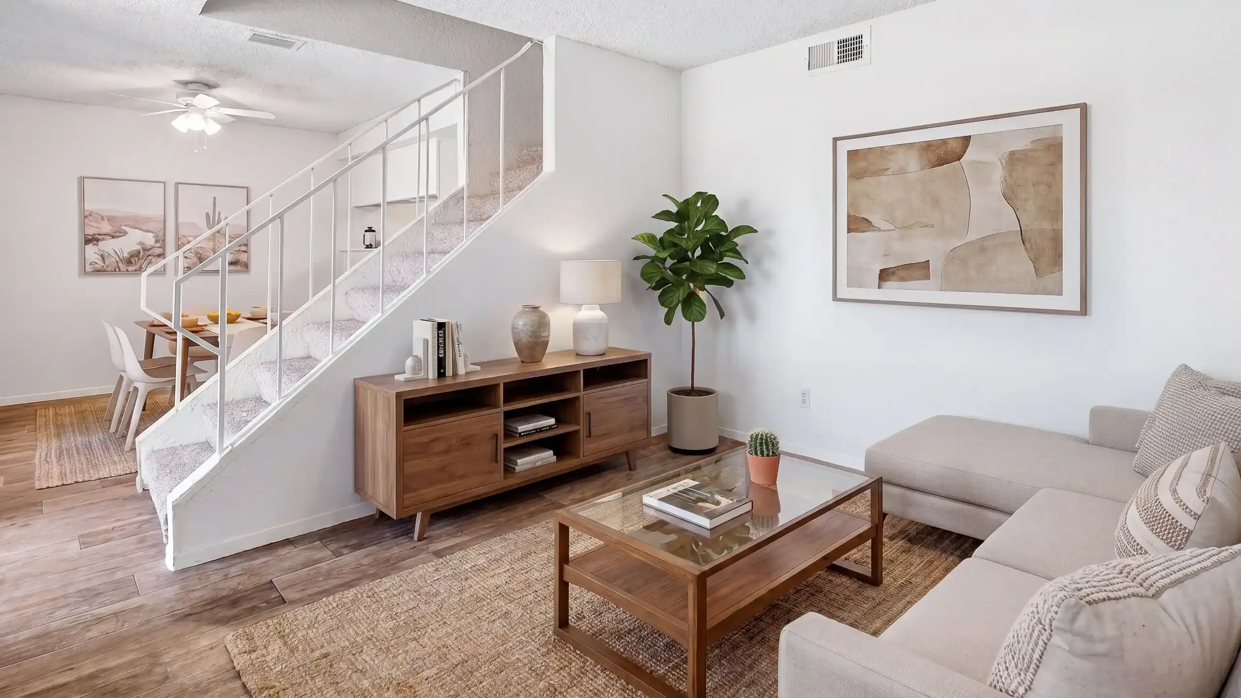Stylish modern living room with light wood flooring, cozy beige sofas, and elegant wooden furniture, complemented by vibrant green plants and a sleek wall-mounted TV.