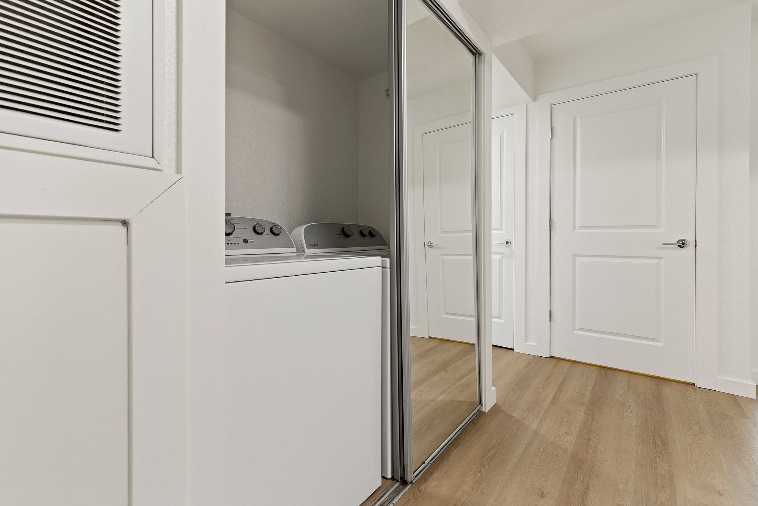 Sleek laundry area in modern apartment with washer and dryer, featuring sliding mirrored doors and elegant wood flooring.