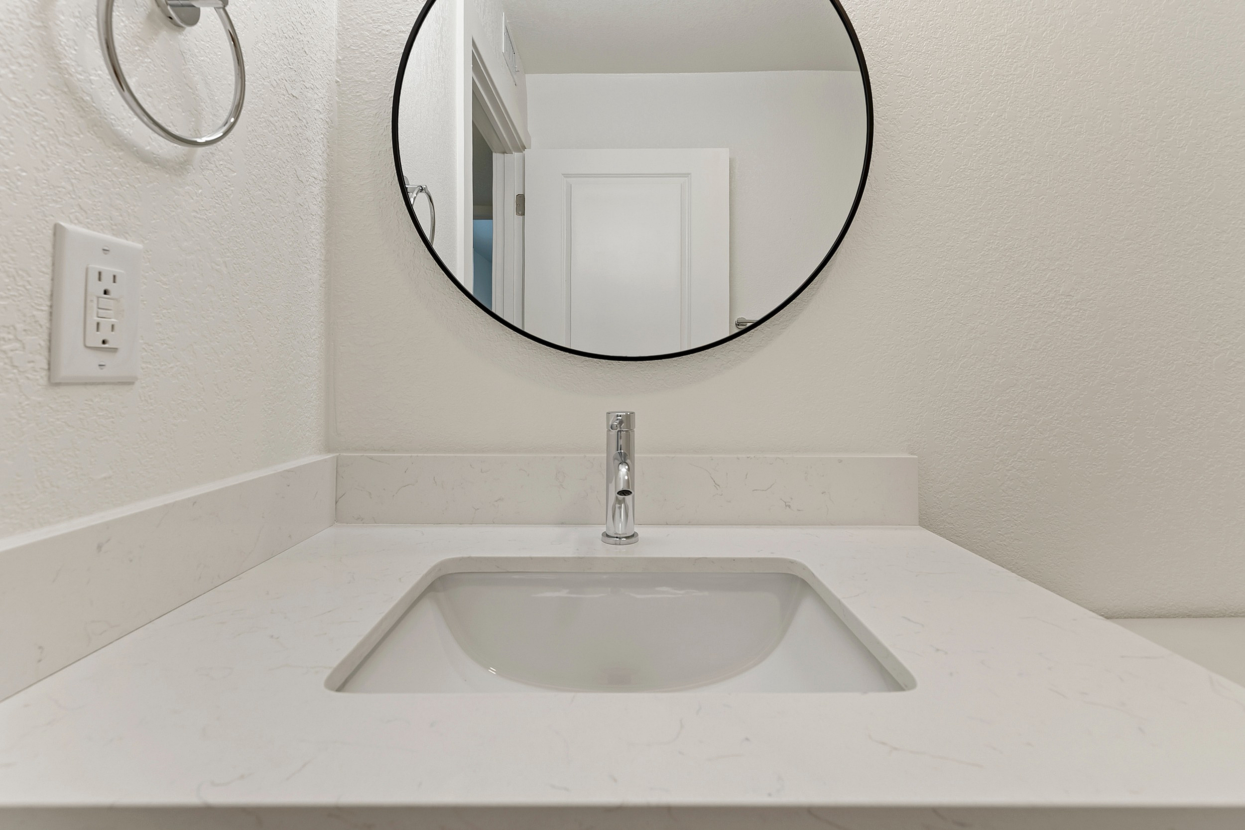 Modern bathroom vanity with sleek white countertop and stylish round mirror, creating a chic and inviting space.