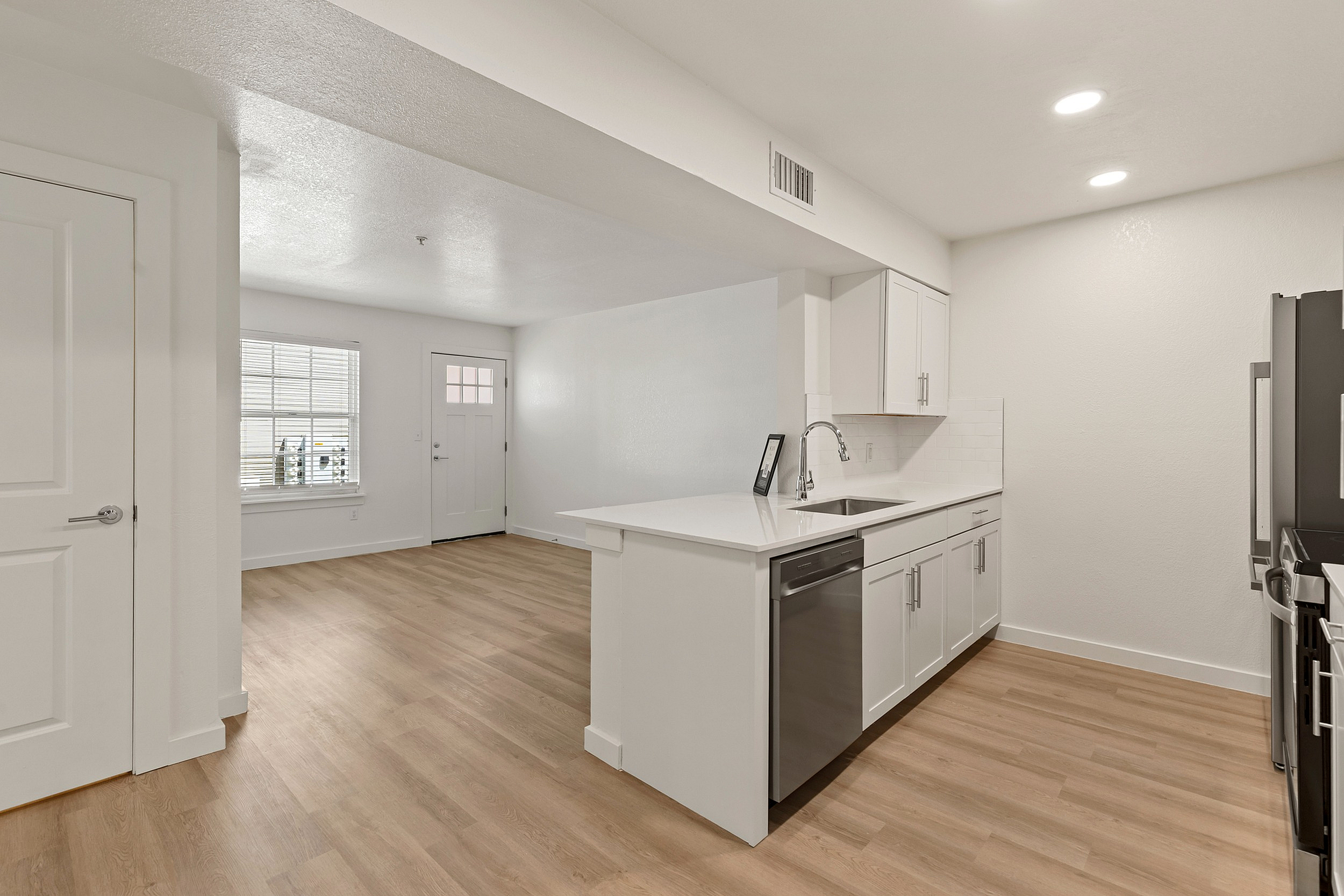 Bright open kitchen with sleek white cabinets, elegant countertops, and modern appliances, showcasing a spacious open floor plan and natural light.