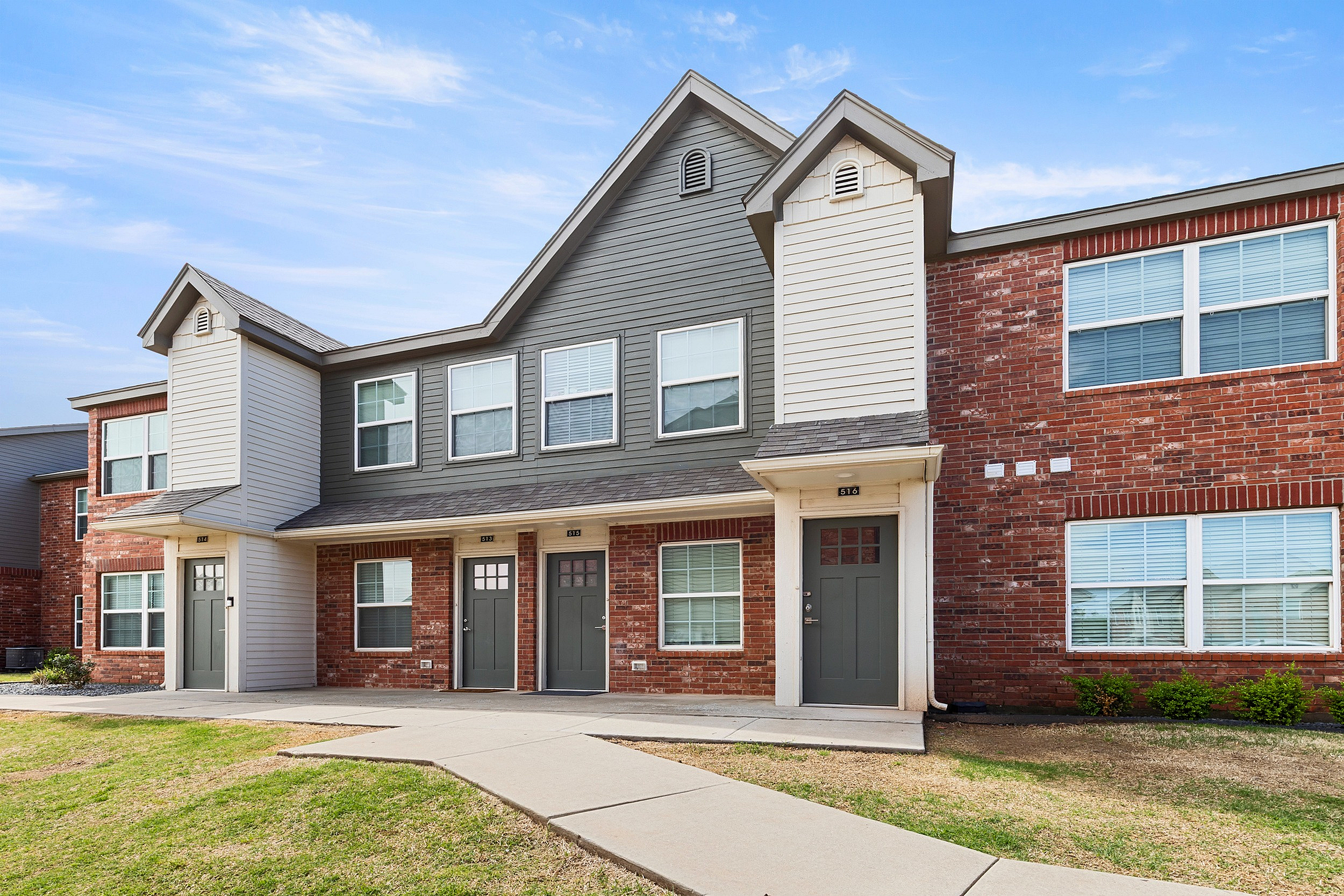 Charming apartment home with modern architecture, featuring red brick and grey siding, set in a peaceful suburban neighborhood.