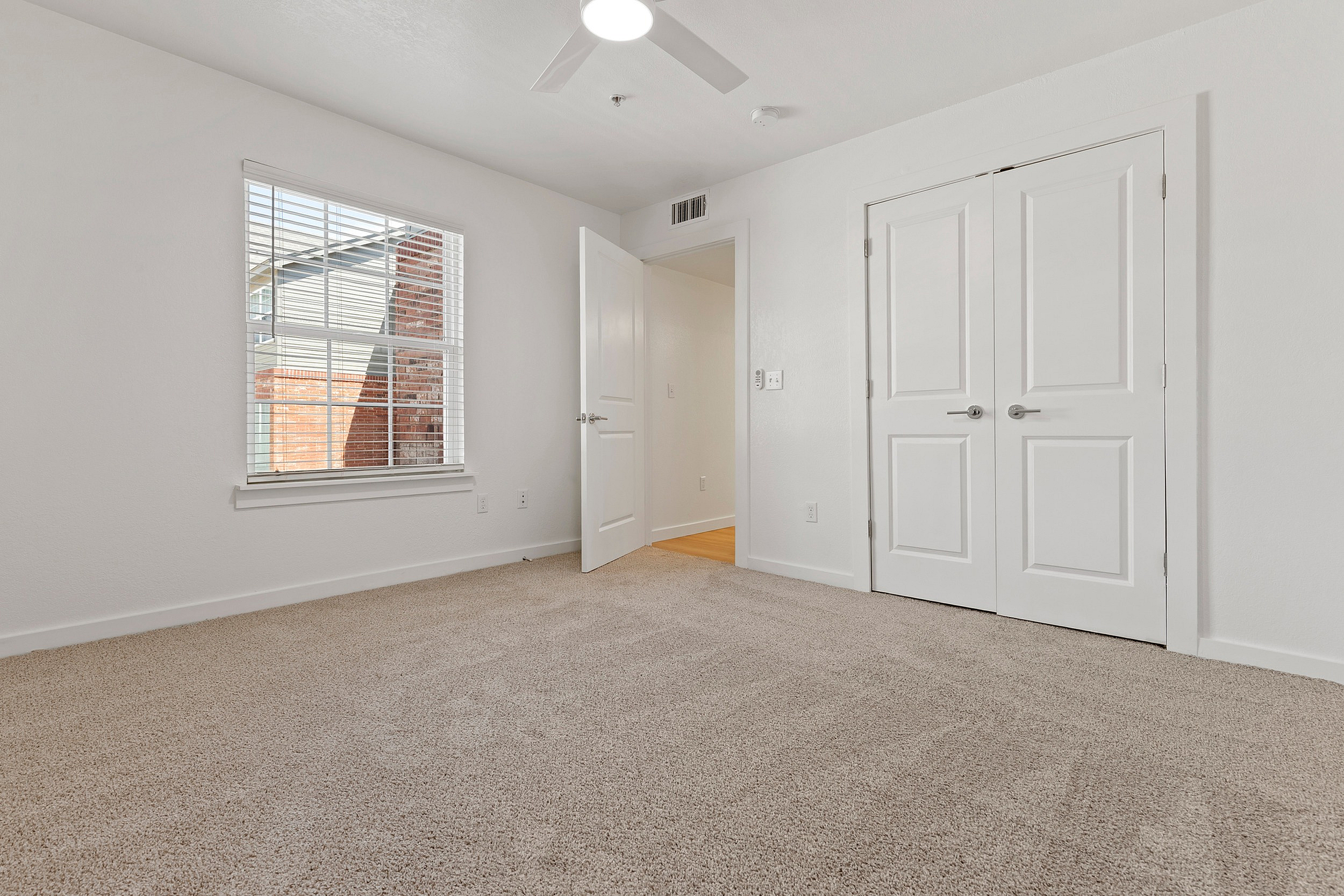 Inviting bedroom with plush carpeting, abundant natural light, and modern white accents.