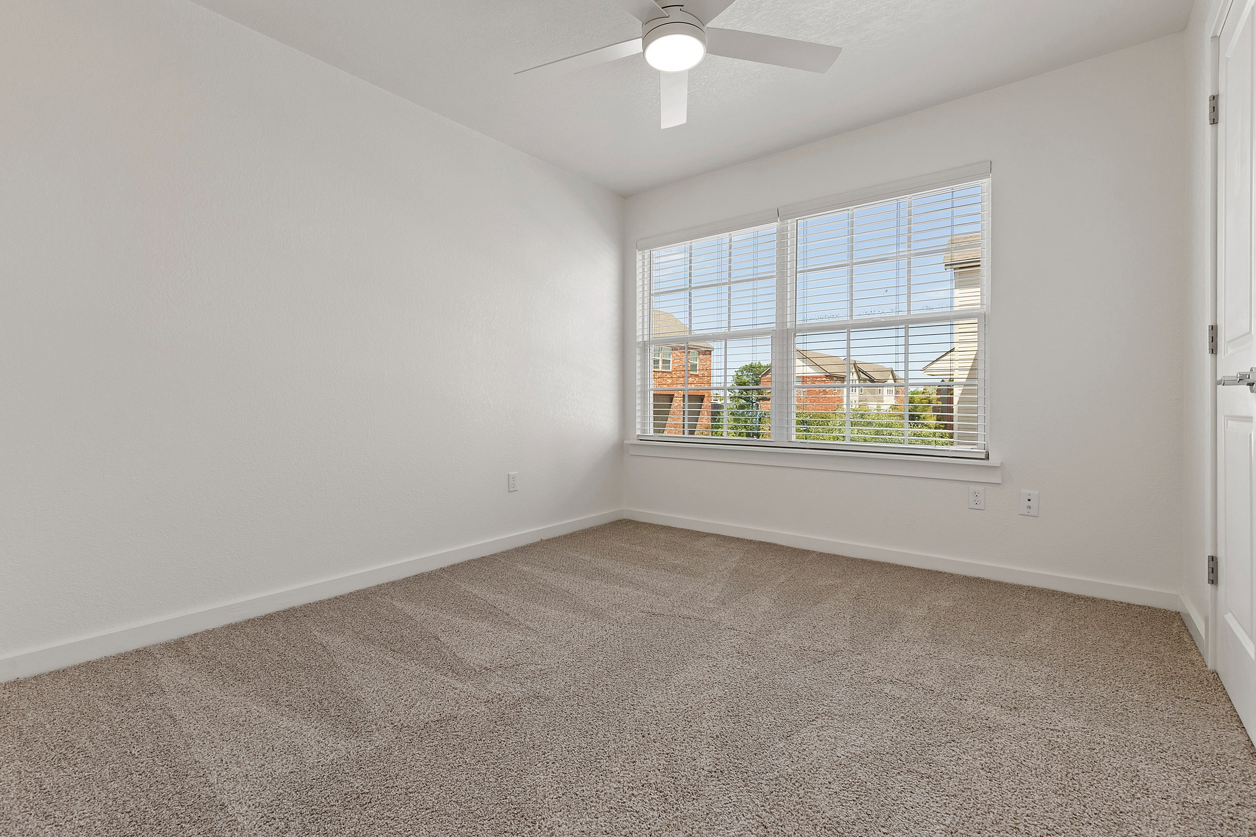 Bright, cozy bedroom featuring plush carpet, a ceiling fan, and large windows with a charming neighborhood view.