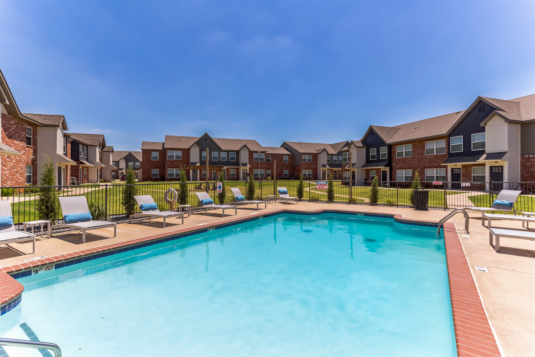 Inviting apartment complex showcasing beautifully landscaped grounds with a sparkling pool and stylish lounge chairs under a clear blue sky.