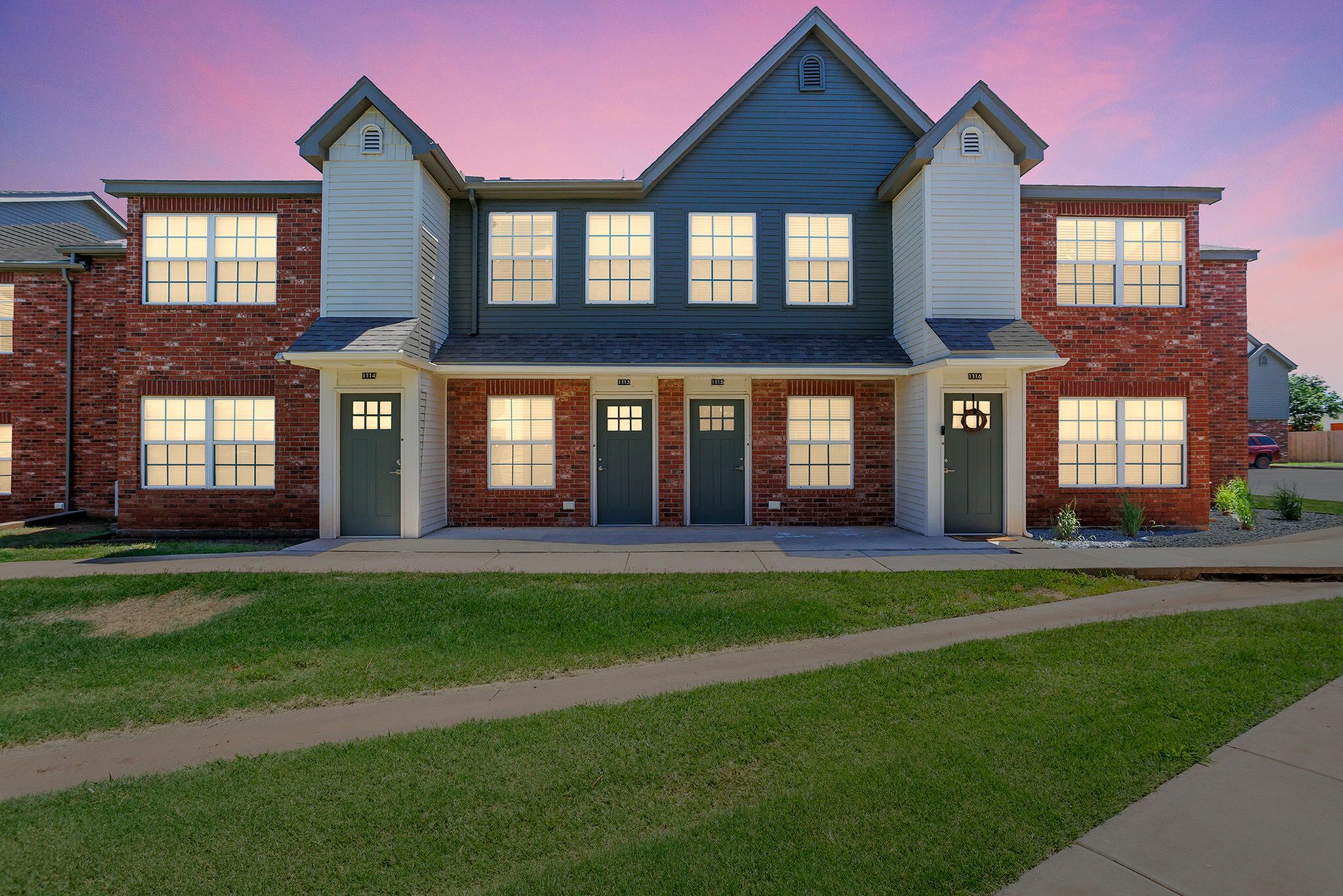 Charming townhouse with red brick facade and inviting entrance, set against a picturesque sunset sky.