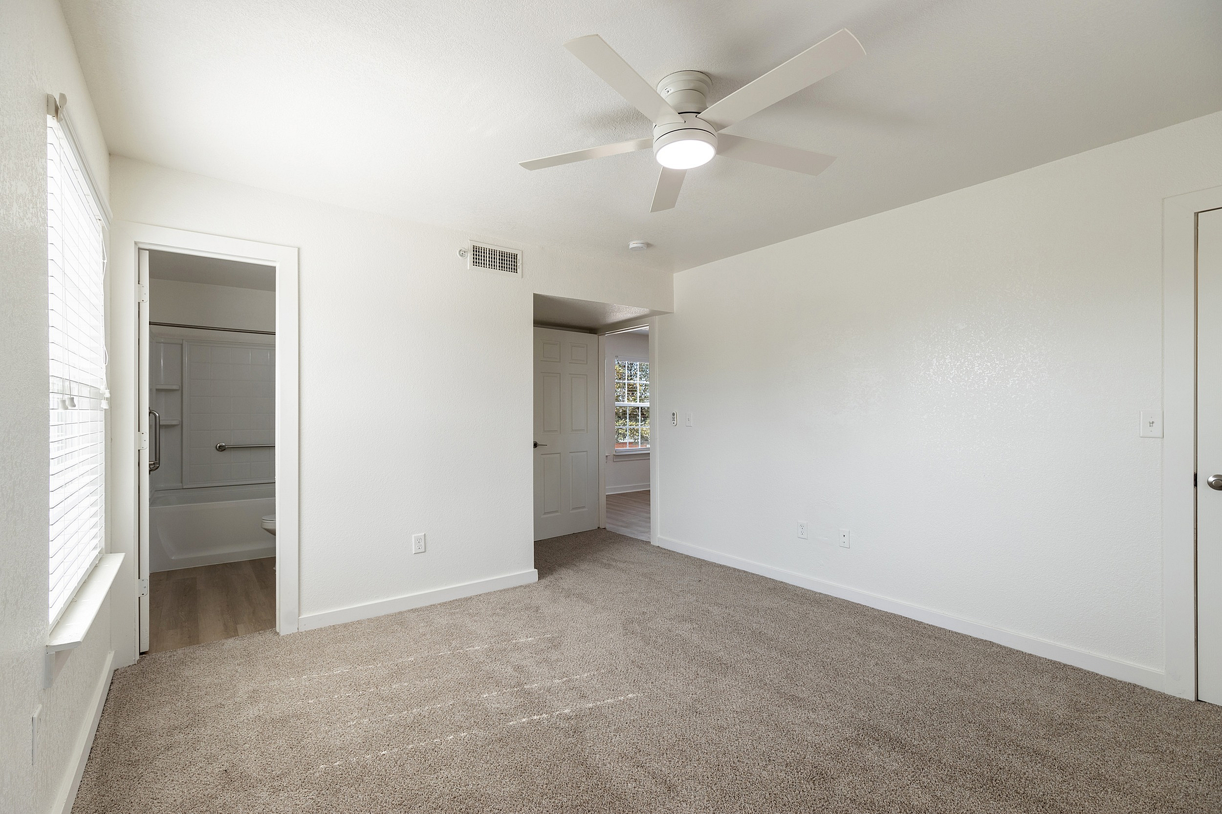 Bright and spacious bedroom with plush carpet, modern ceiling fan, and ensuite bathroom access.