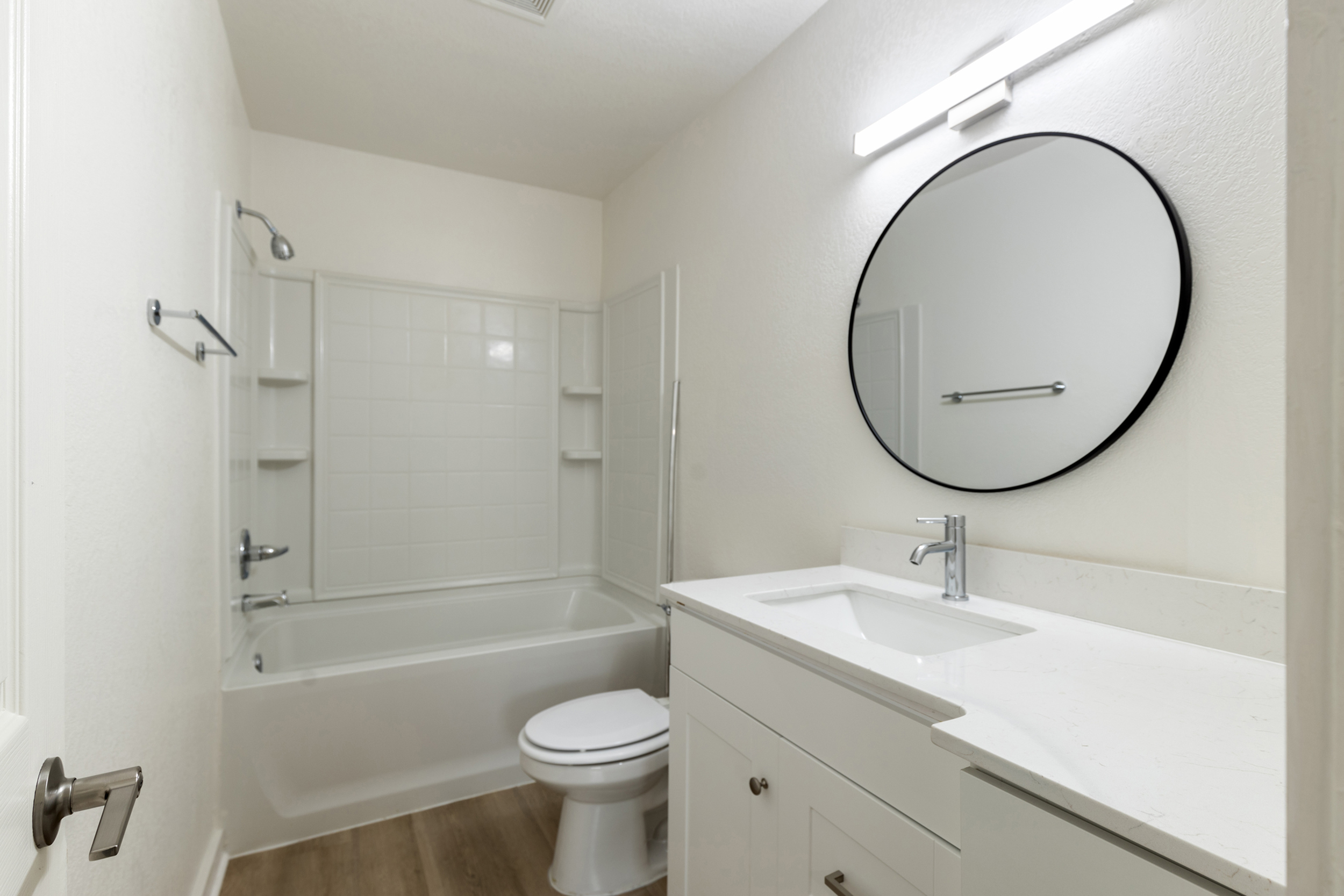 Modern bathroom featuring sleek white vanity, circular mirror, and pristine bathtub with neutral tones.