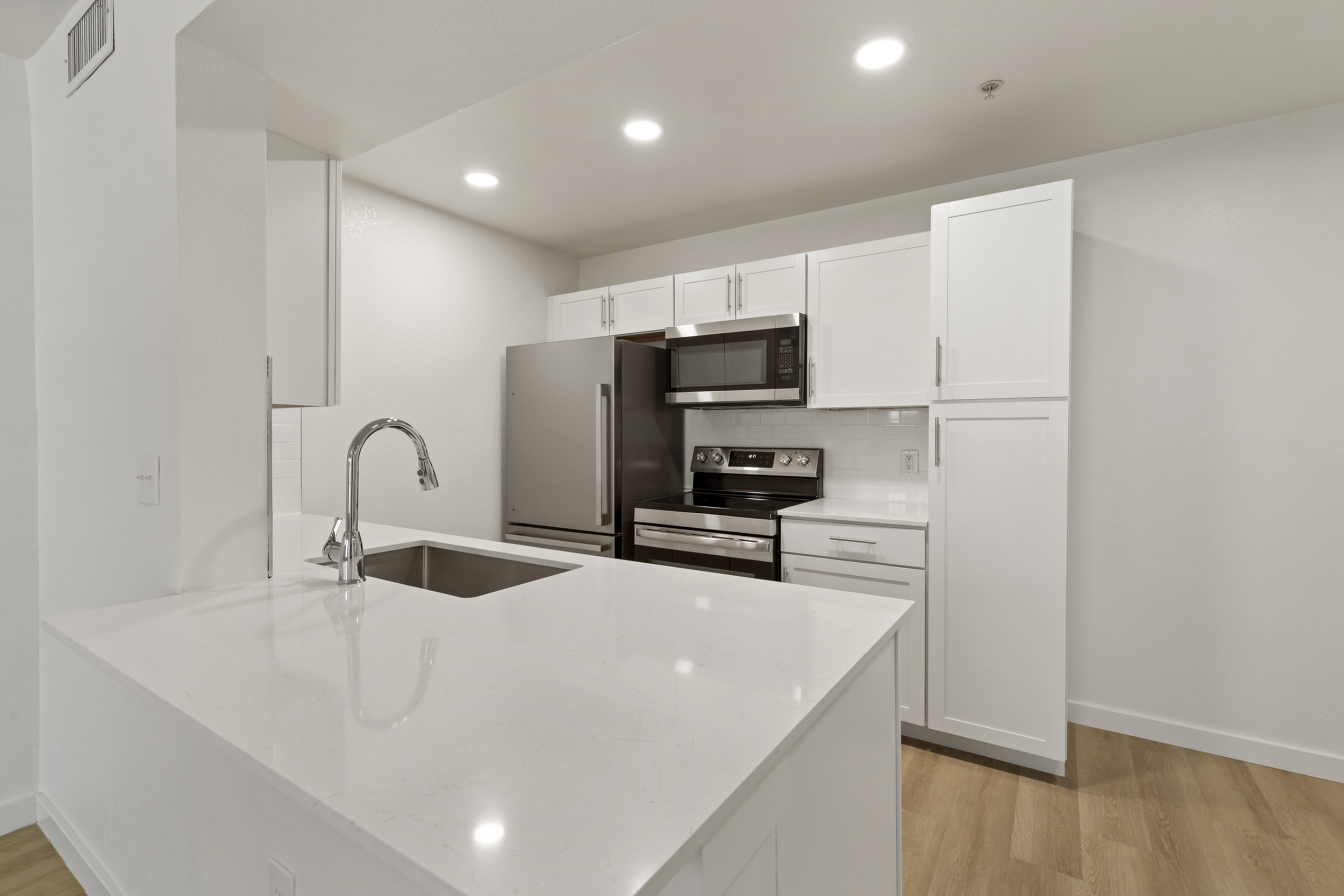 Modern kitchen with sleek white cabinetry, stainless steel appliances, and a polished quartz countertop.