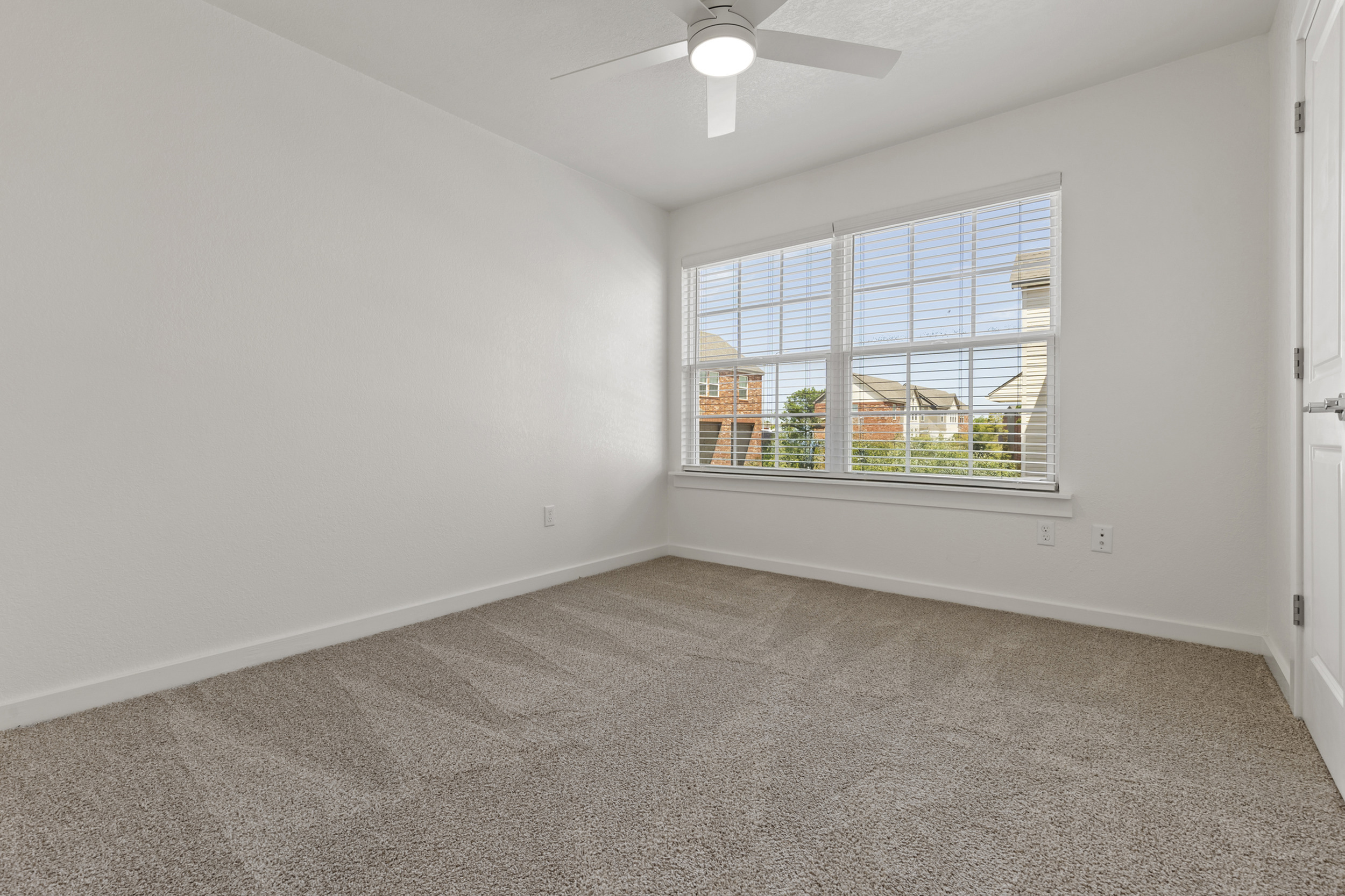 Bright bedroom with plush carpet, large window offering natural light, and a ceiling fan for comfort.
