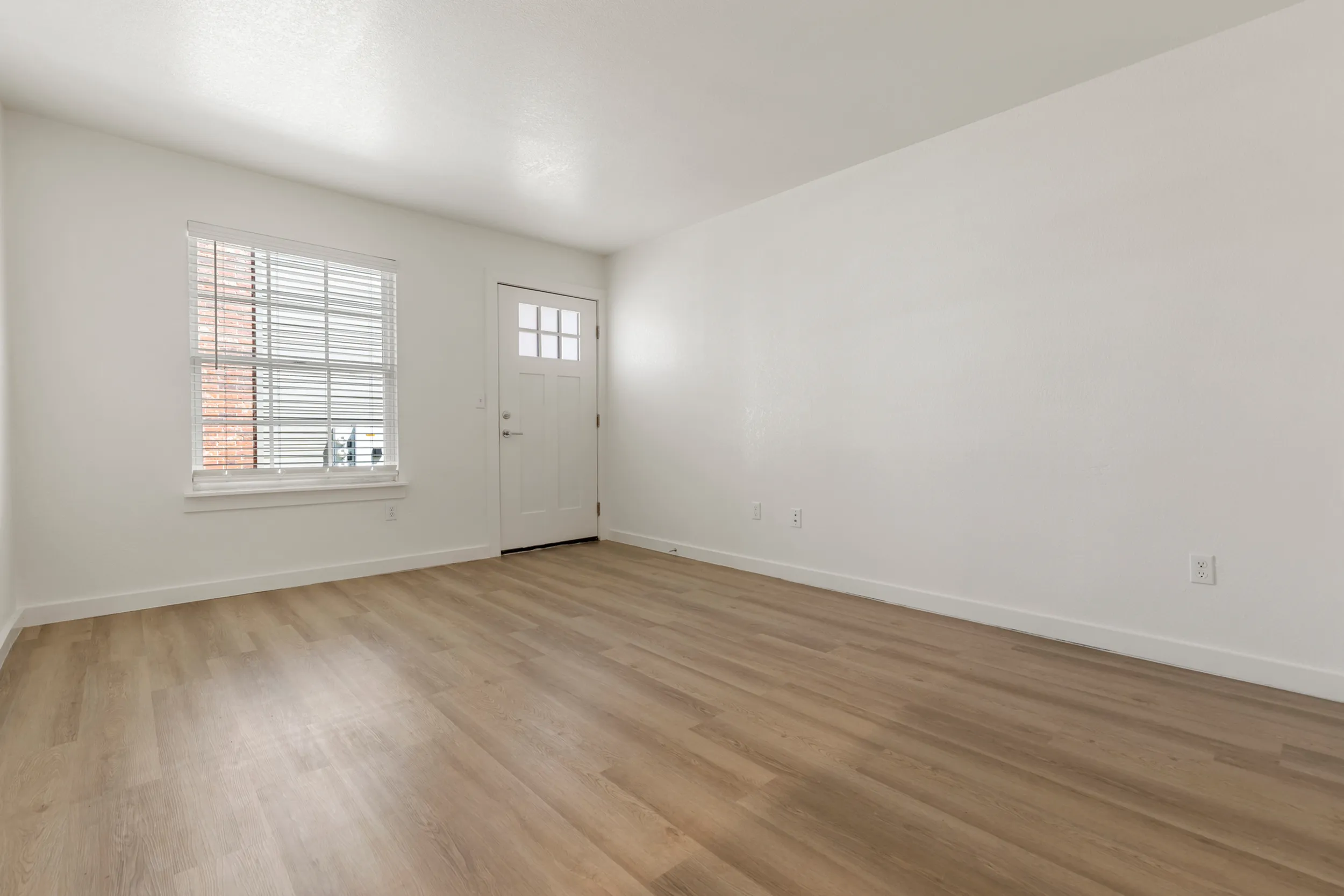 Bright living space with sleek hardwood flooring and natural light pouring in from a large window and a stylish door.