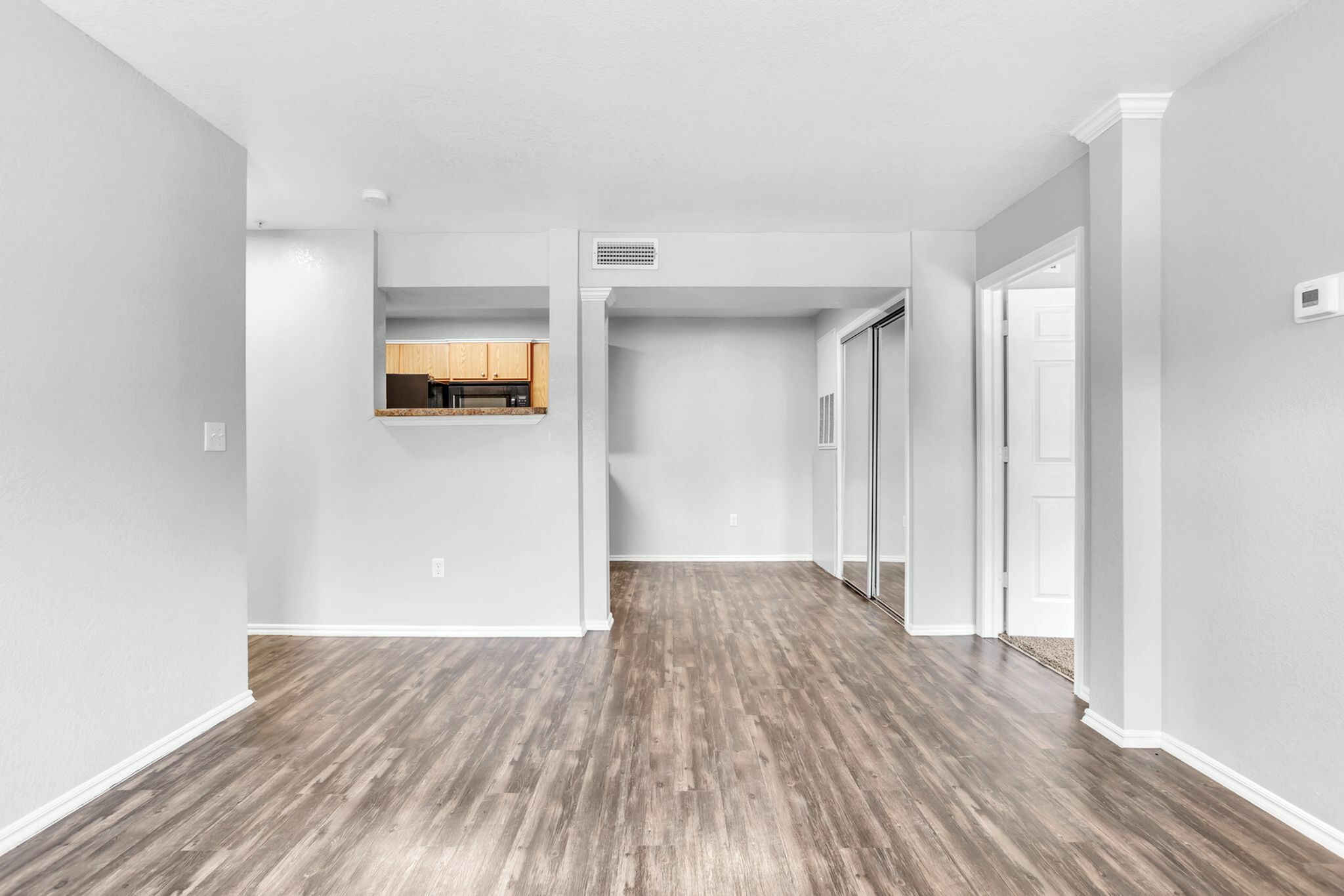 Modern open-plan apartment with elegant flooring, bright neutral walls, and a glimpse into a cozy kitchen area.