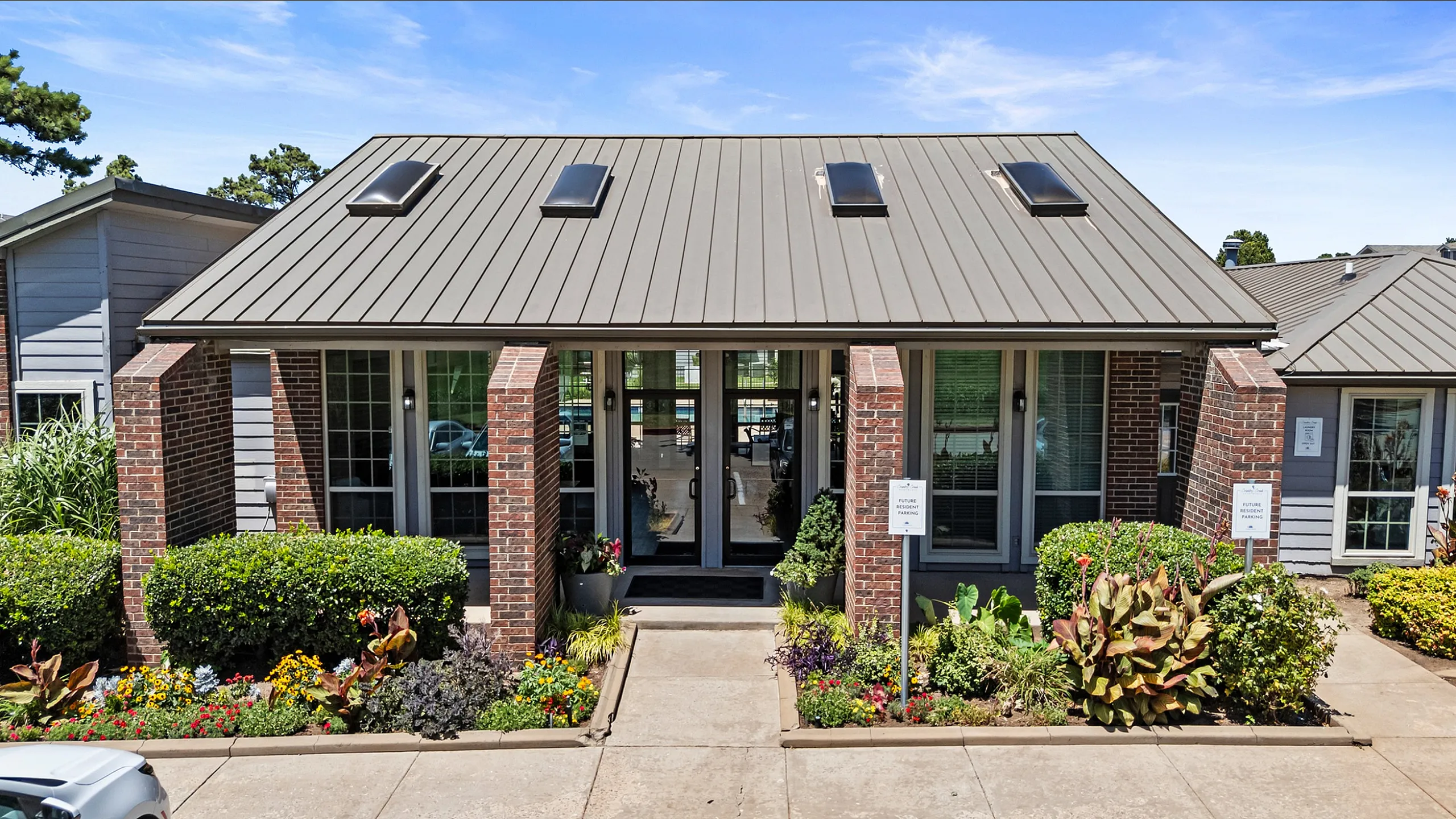 Charming brick home with modern metal roof, inviting entryway, and vibrant garden landscaping.