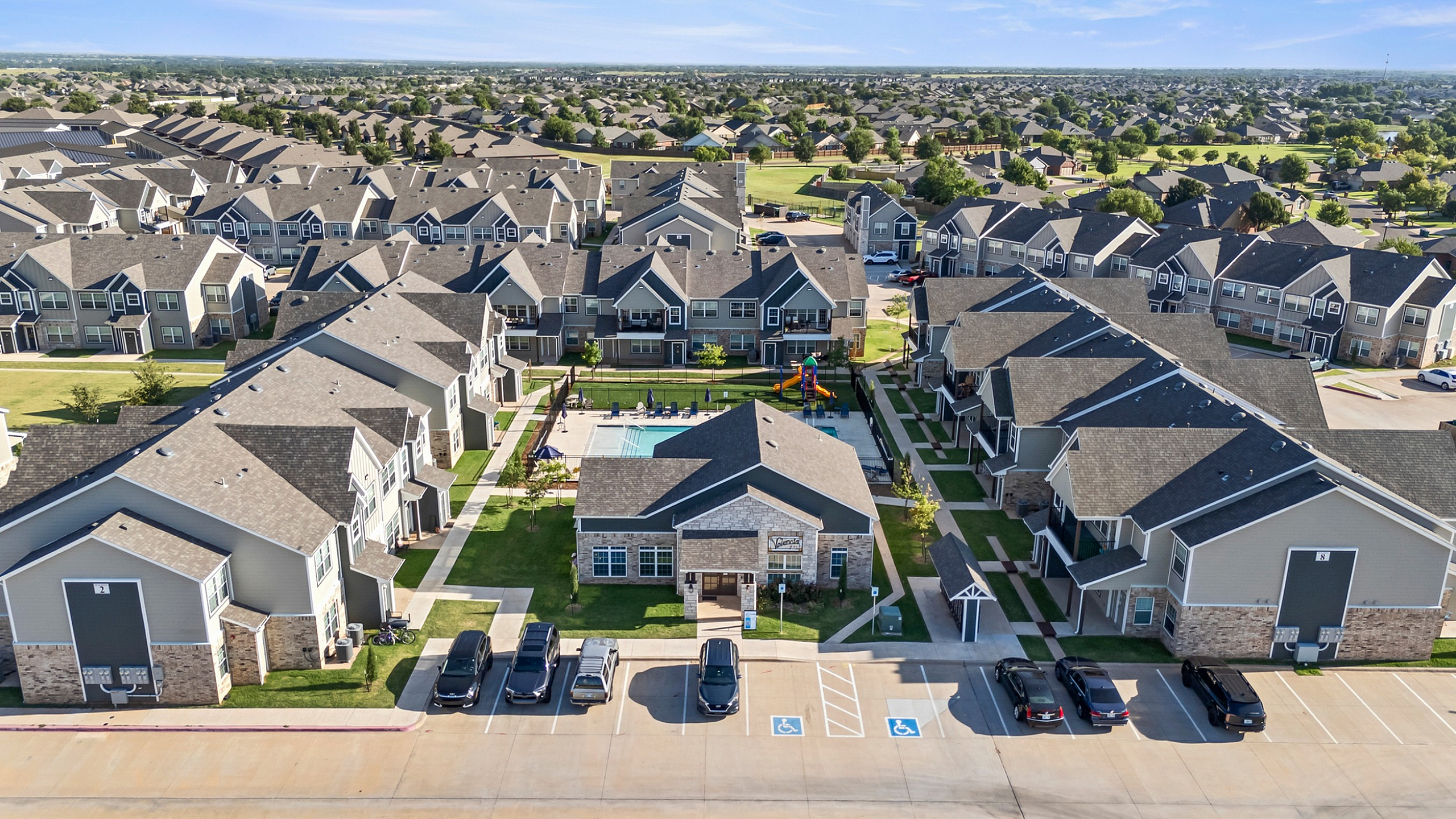 Charming apartment complex featuring modern duplexes, lush green spaces, and a central pool area with a playground, ideal for family living.