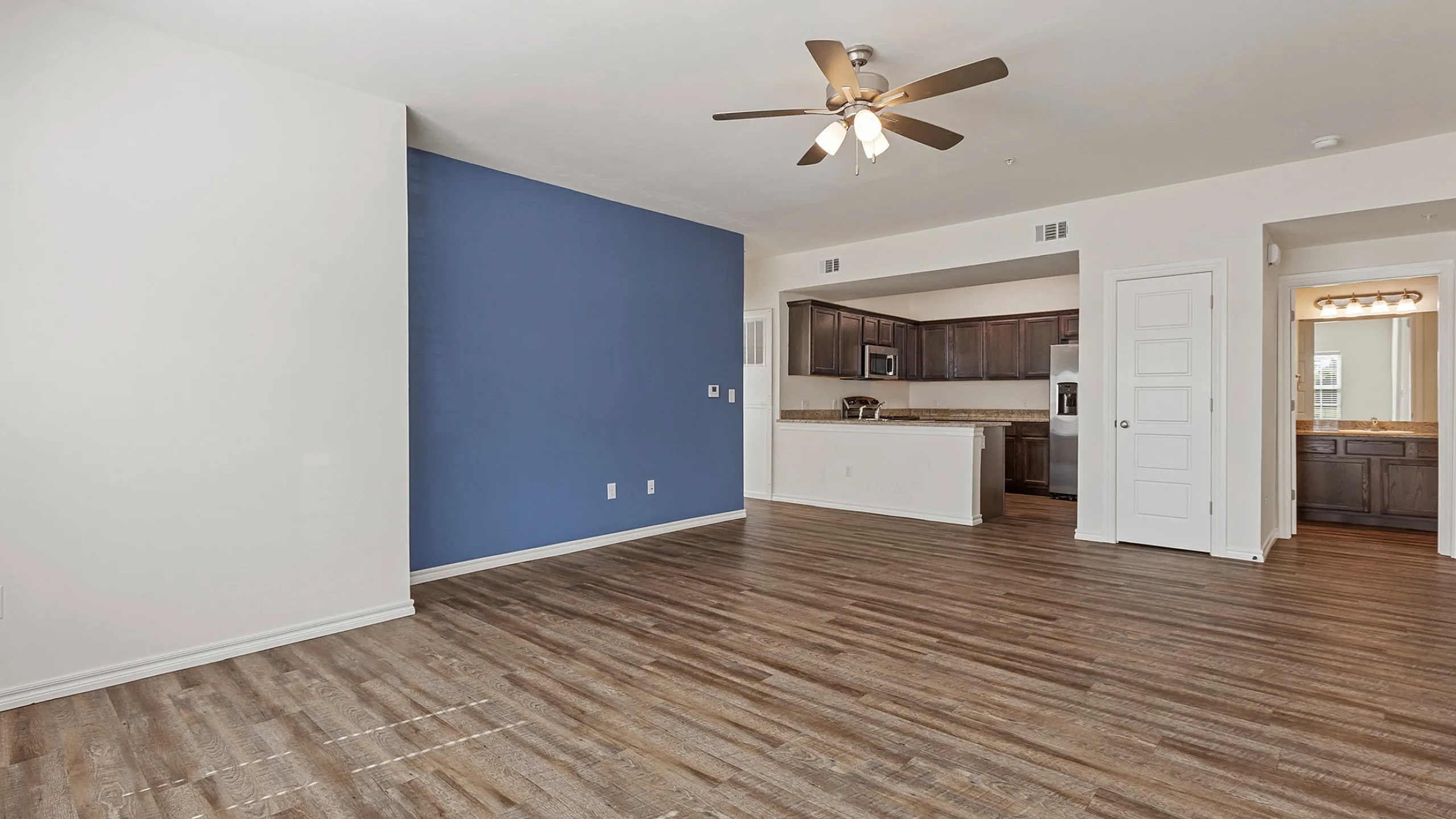 Spacious open-plan living area with elegant hardwood flooring, modern ceiling fan, and a stylish kitchen featuring dark wood cabinets and granite countertops.