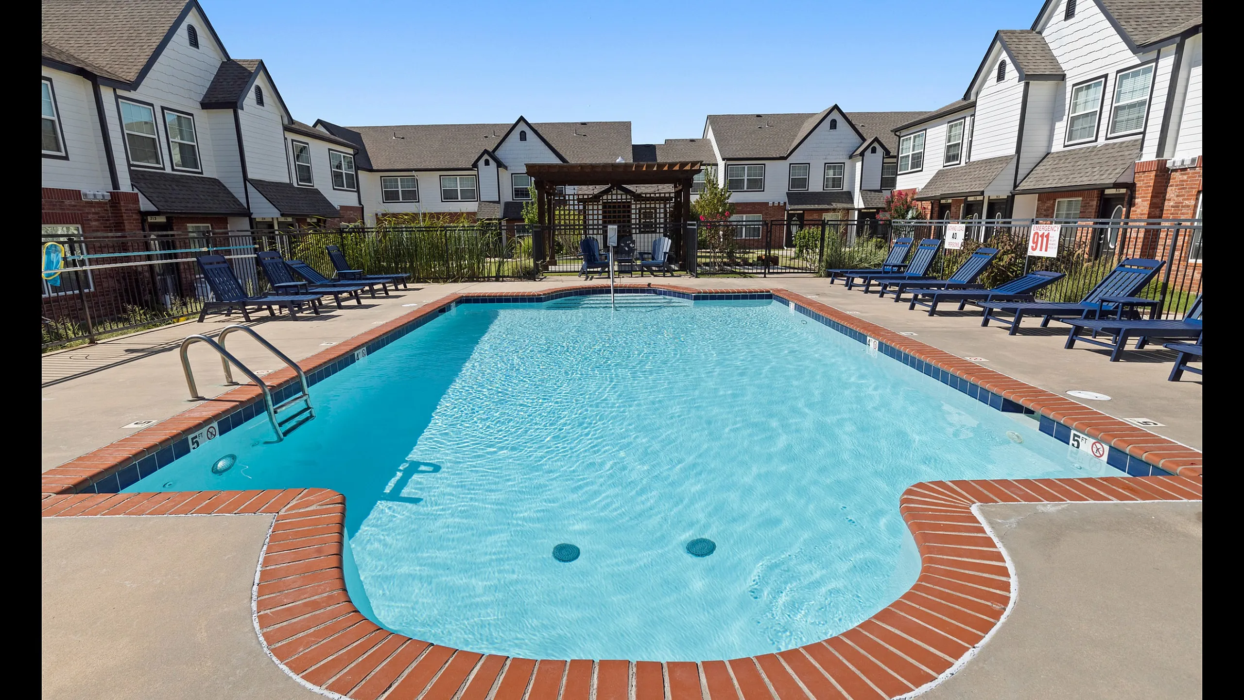 Inviting outdoor pool area surrounded by modern townhouses, featuring comfortable lounge chairs and a charming pergola.