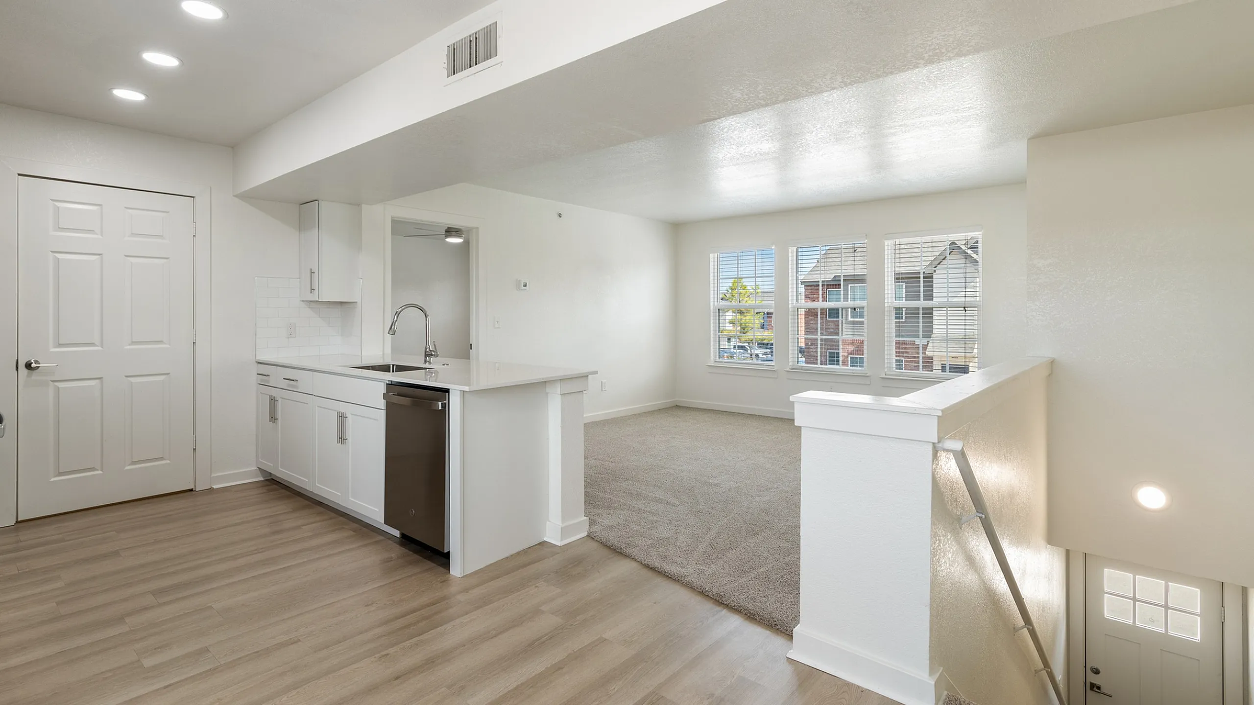 Bright and modern open-plan living space featuring a sleek kitchen with stainless steel appliances and a sunlit living room with large windows.