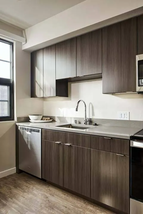Closeup of sink in sunlight with grey counters and wood-inspired cabinets