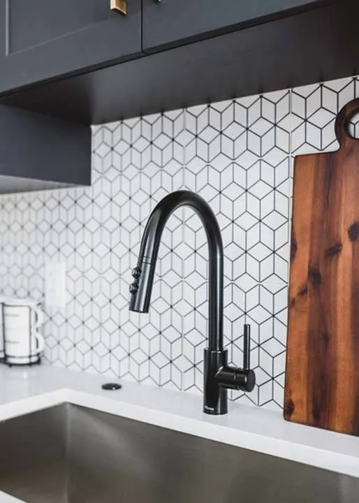 Closeup of faucet with stylish mosaic tile backsplash beyond