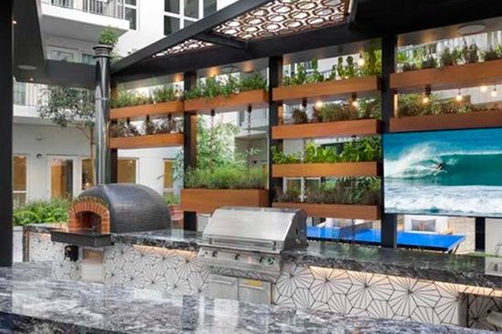 Outdoor kitchen featuring vertical green wall, pizza oven, TV and grilling station with bar seating area