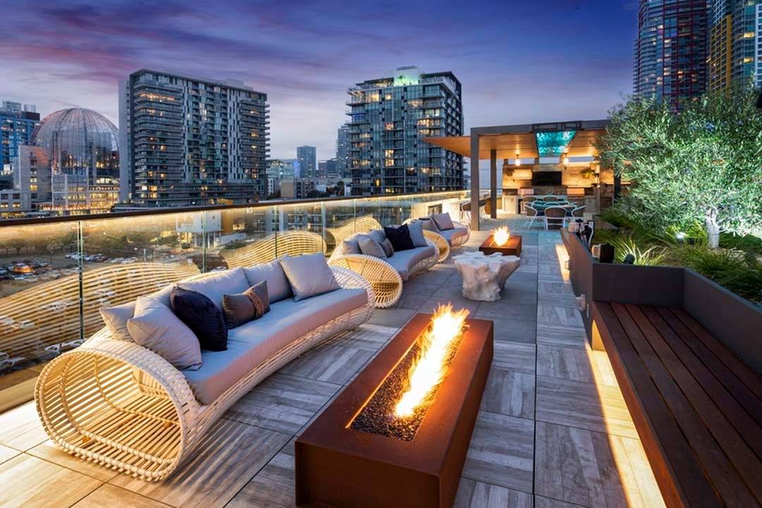 Firepits and lounge seating line the edge of the rooftop pool deck with city lights behind them