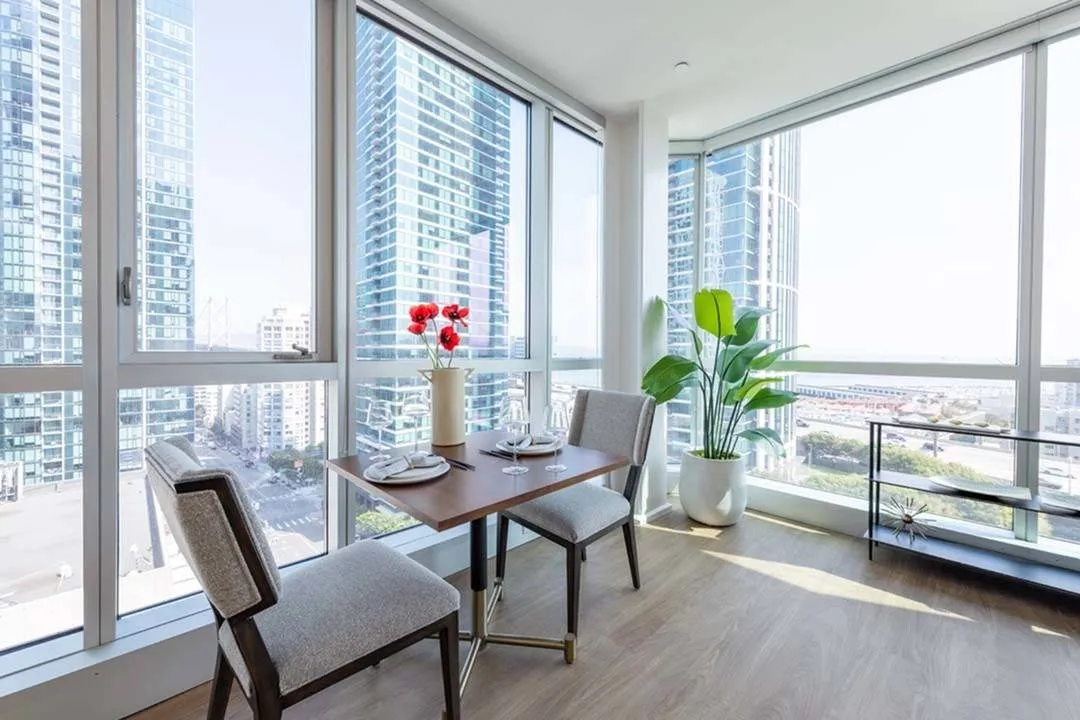Table for 2 and bookshelf in front of a floor-to-ceiling window looking out at the city and bay