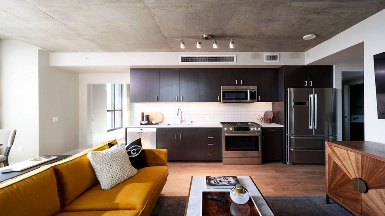 Stunning stainless steel appliances and elegant cabinetry behind an open living room with concrete ceiling