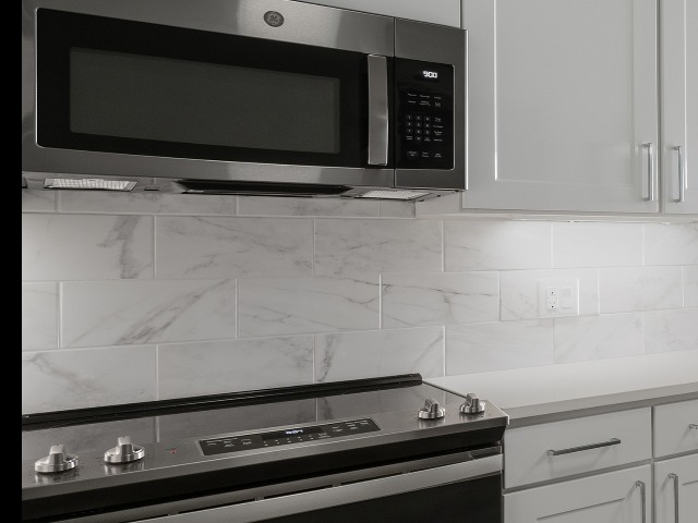 Close up shot of white tile backsplash above stove and below white countertops