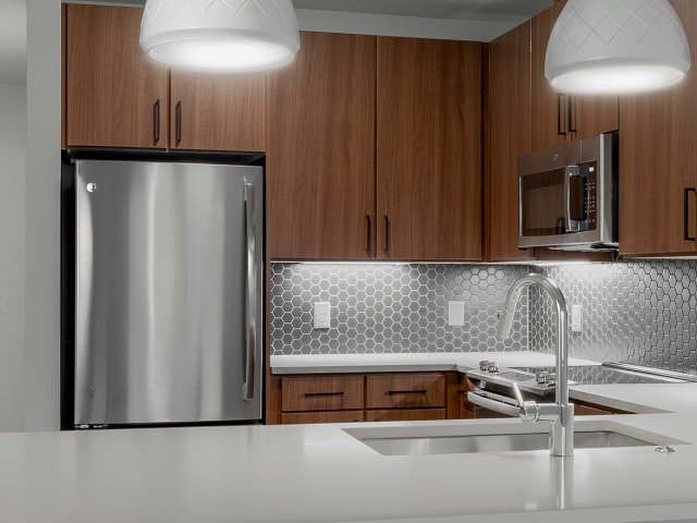 Close up of the dark wood kitchen color palette showing stainless steel appliances, white countertop, and lights over island