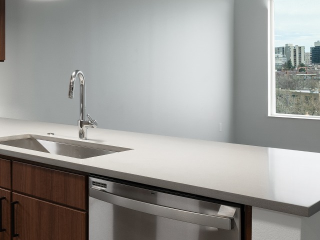 Close up of kitchen sink and white countertop looking over living room with a window in the background