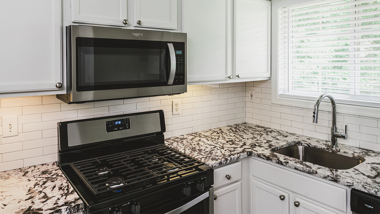 Modern upgraded kitchen with granite counter, white cabinets and stainless microwave and range