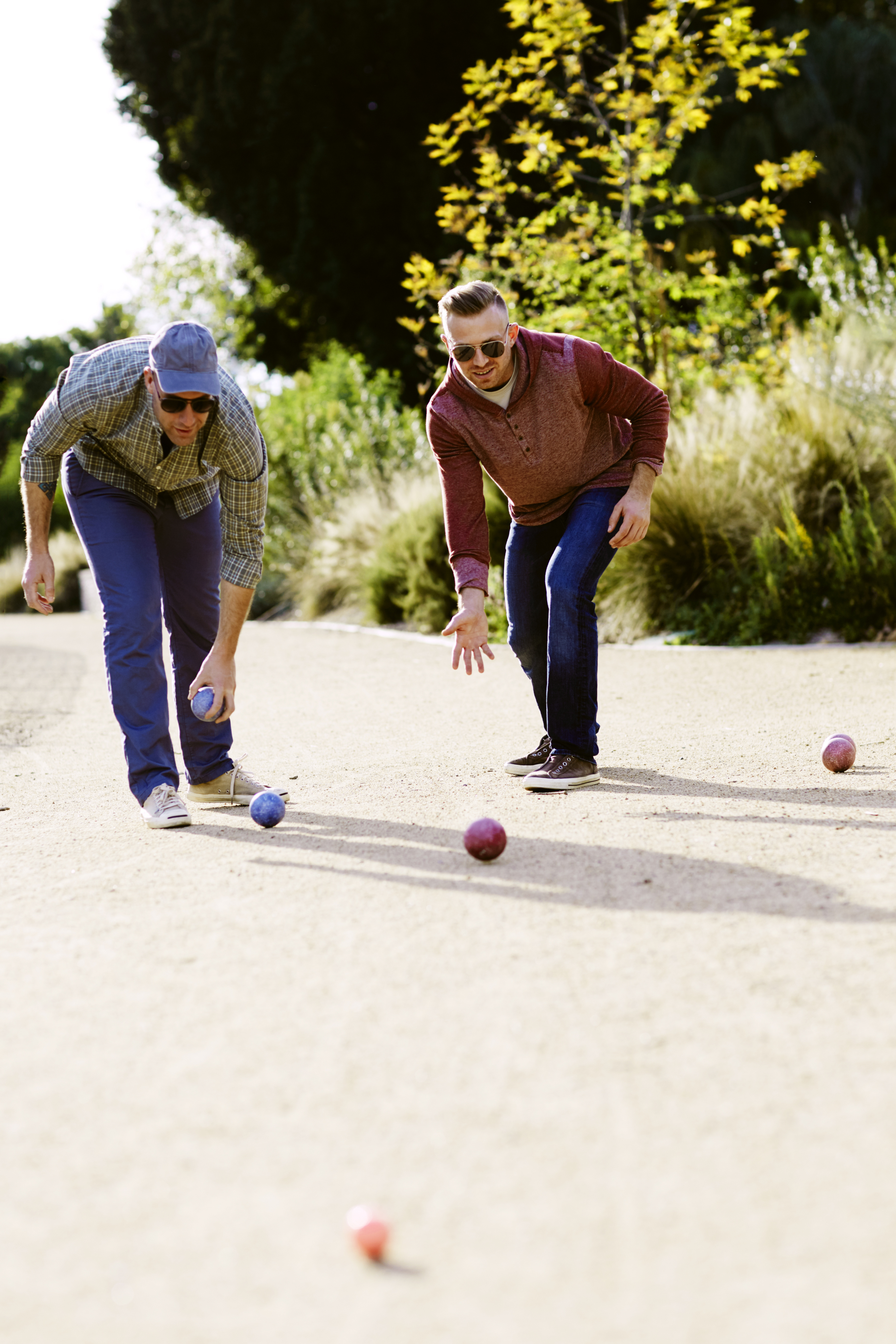Two friends enjoying a lively game of bocce on a sunny day, surrounded by lush greenery.