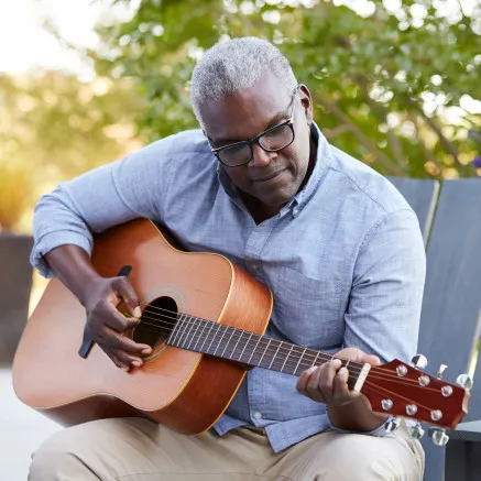 Man outside playing guitar while sitting in chair