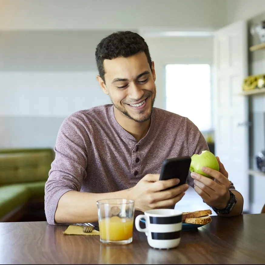 young adult man sitting at table scrolling on phone over breakfast