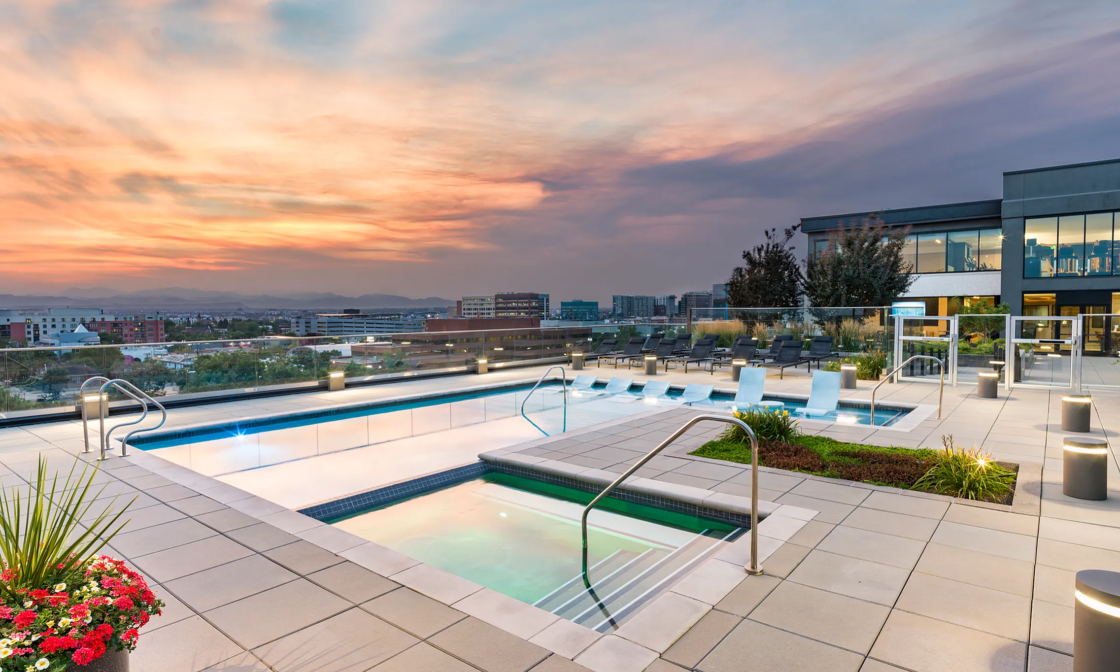 Luxurious rooftop pool area with scenic city and sunset views, featuring modern loungers and vibrant landscaping.