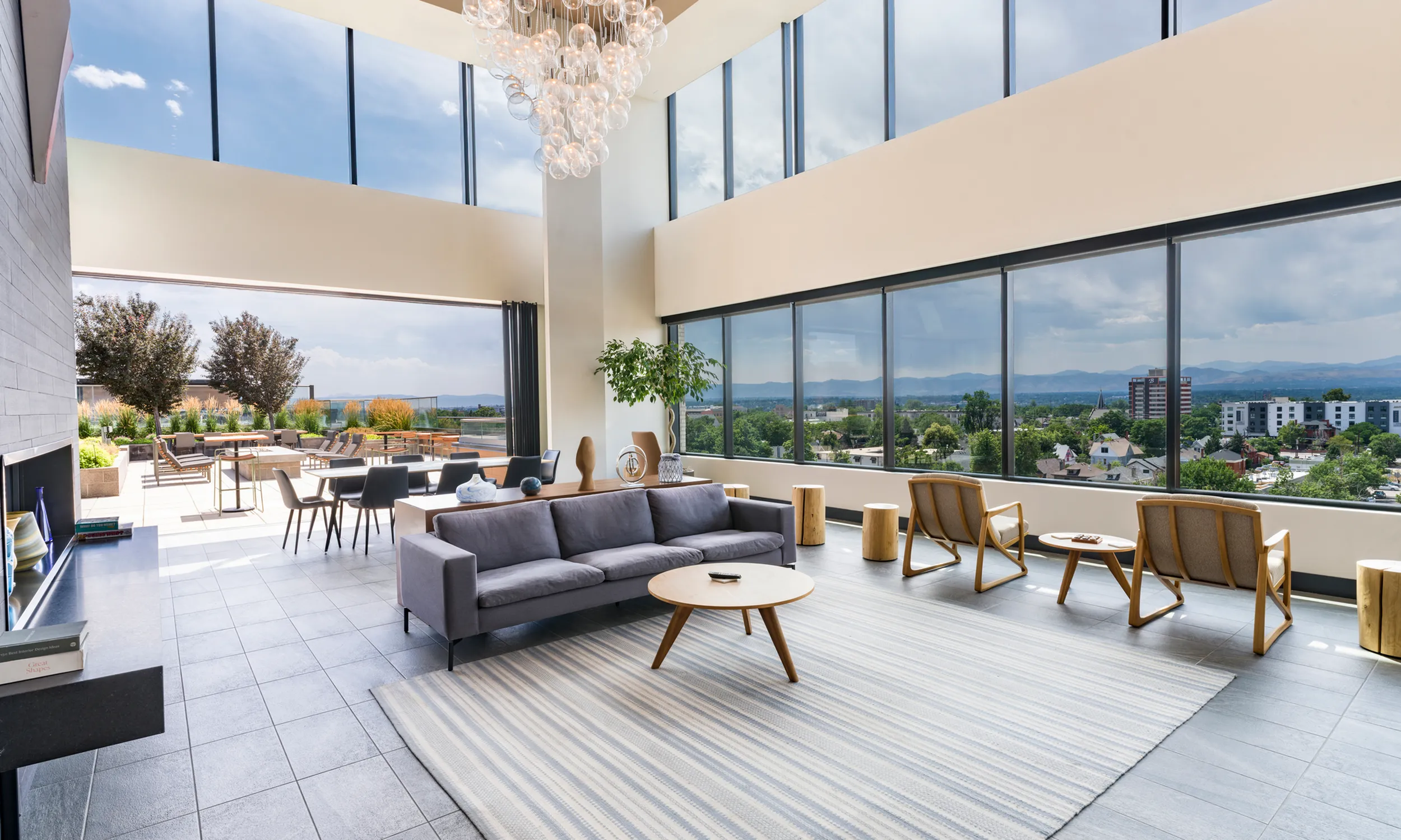 Luxurious living area with floor-to-ceiling windows showcasing a breathtaking cityscape and mountain views, featuring chic modern furniture and an elegant chandelier.